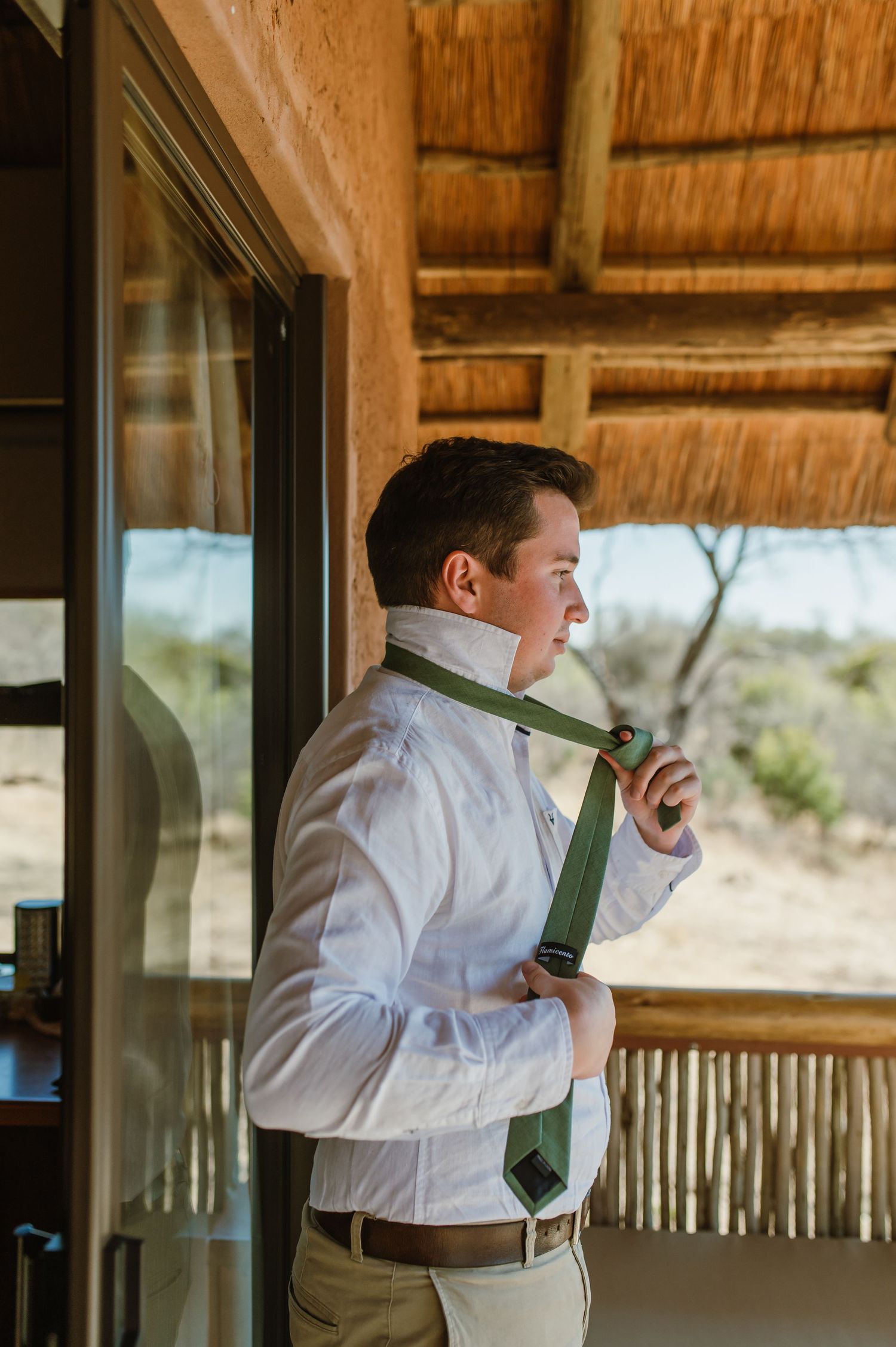 Person putting on green tie while standing in covered outdoor deck.