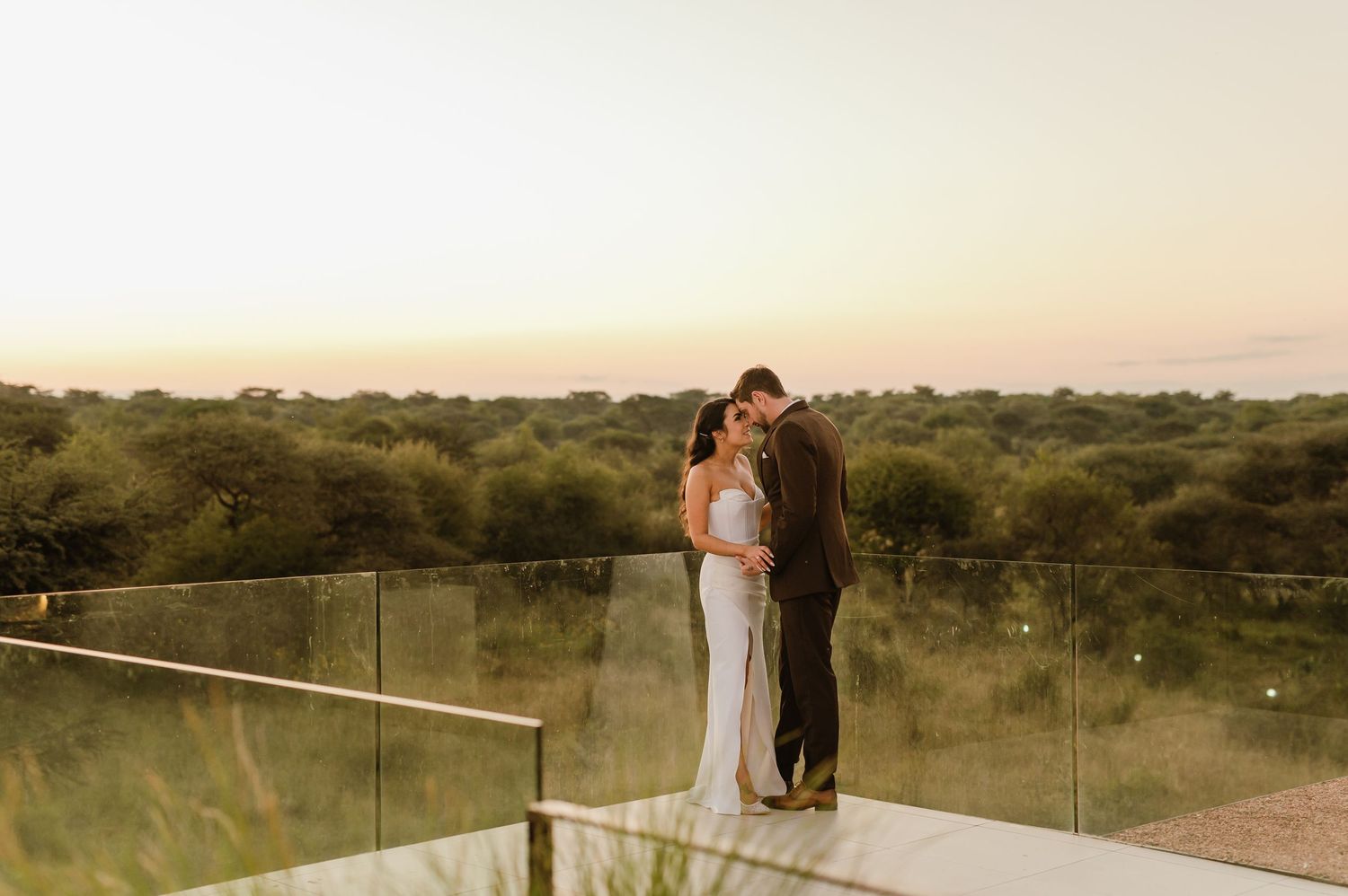 Romantic silhouette of couple embracing on balcony overlooking natural landscape at dusk.