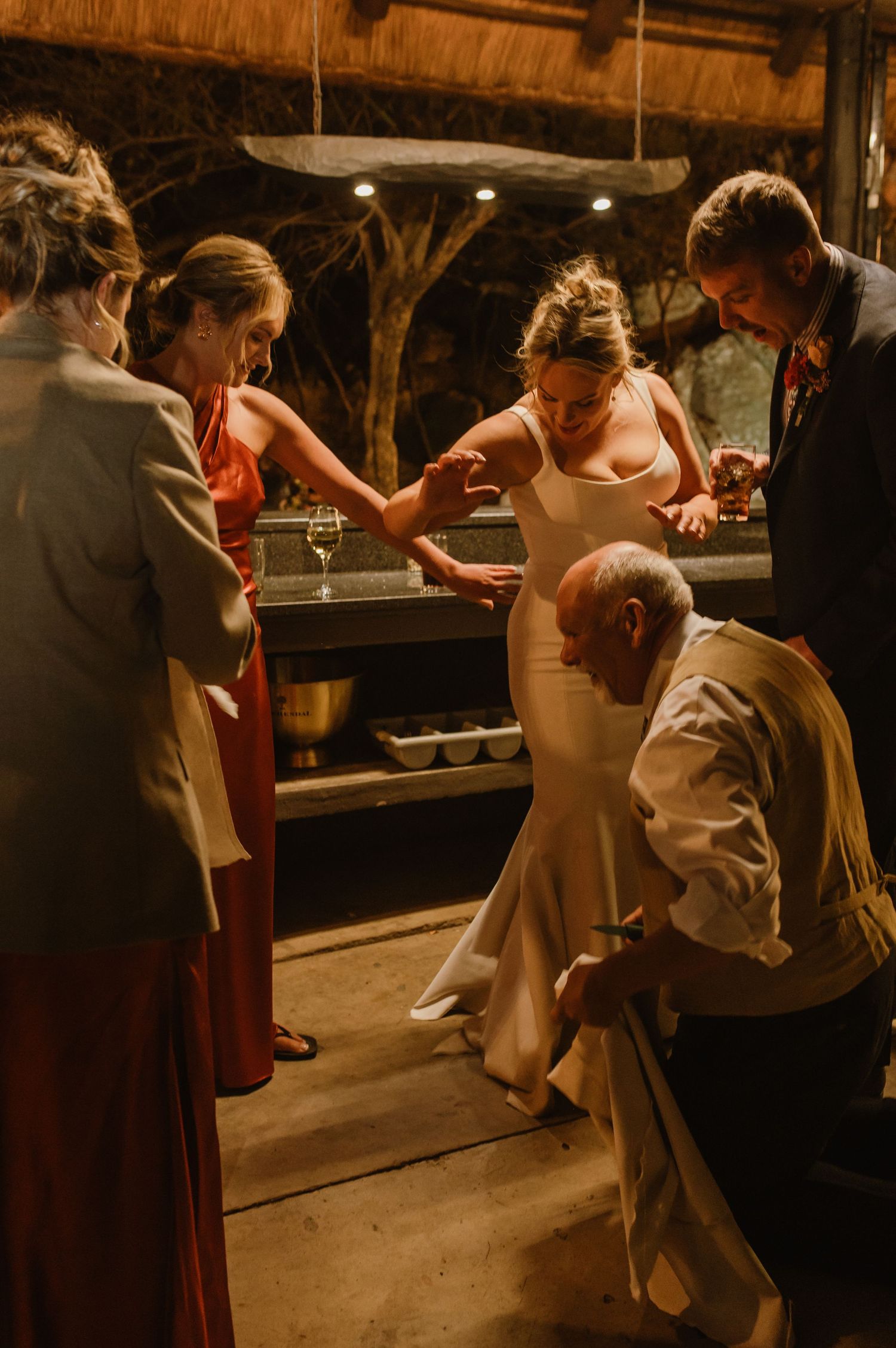 Wedding guests help adjust the bride's dress during reception celebrations.