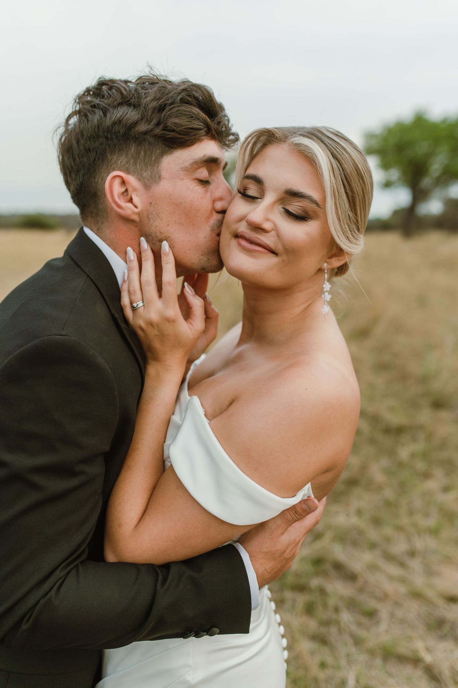 A tender moment between newlyweds captured in a sun-lit field during their wedding.