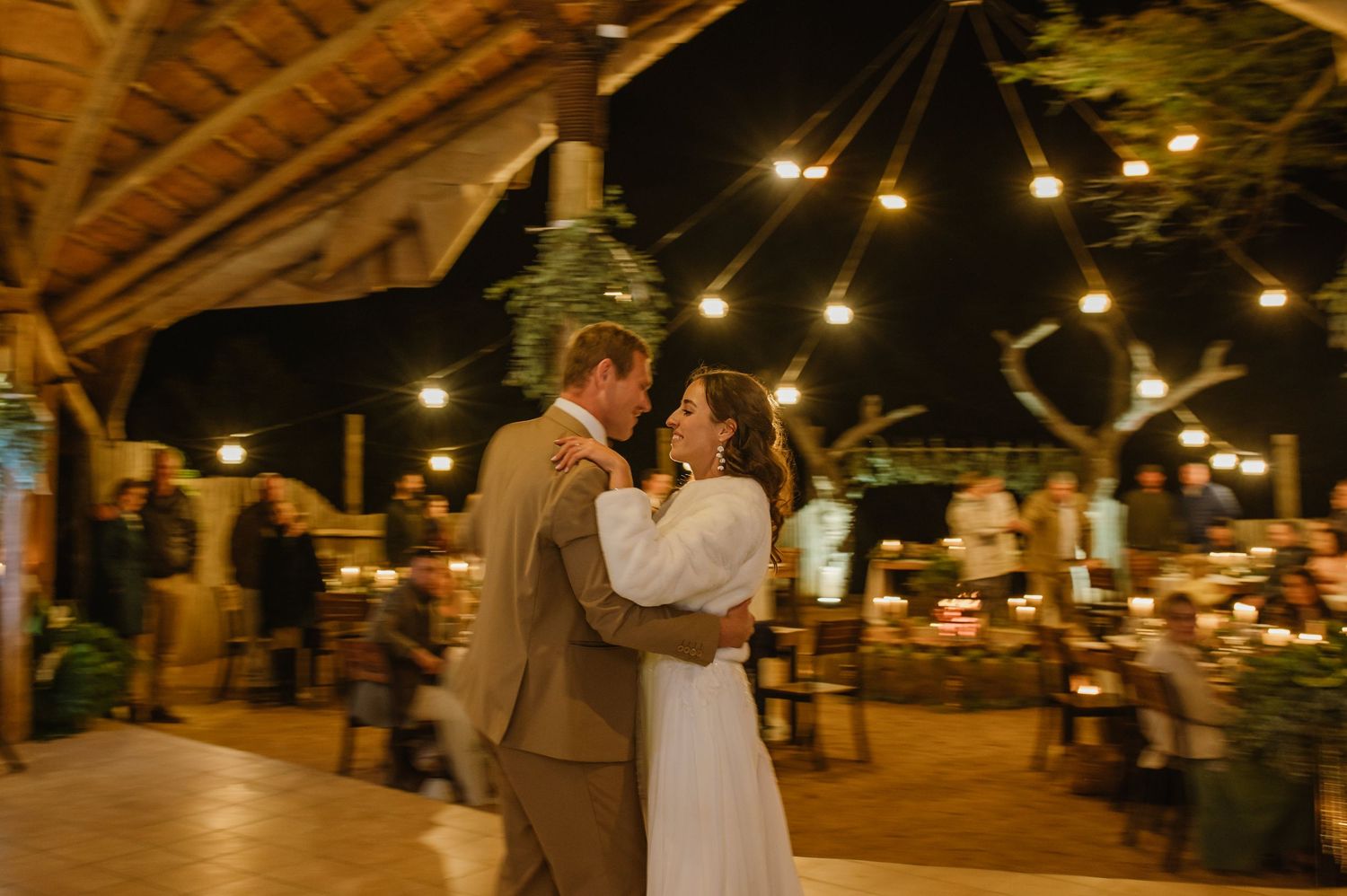 An outdoor wedding reception venue decorated with string lights and rustic wooden beams.