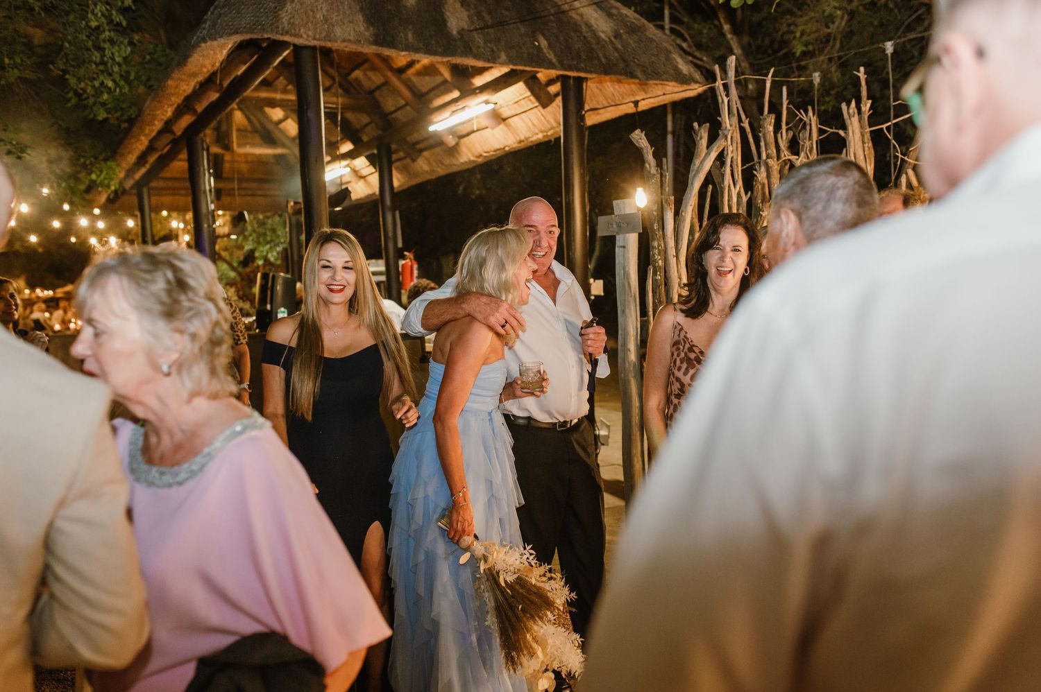 Wedding party dancing and celebrating under covered outdoor venue with ambient lighting.