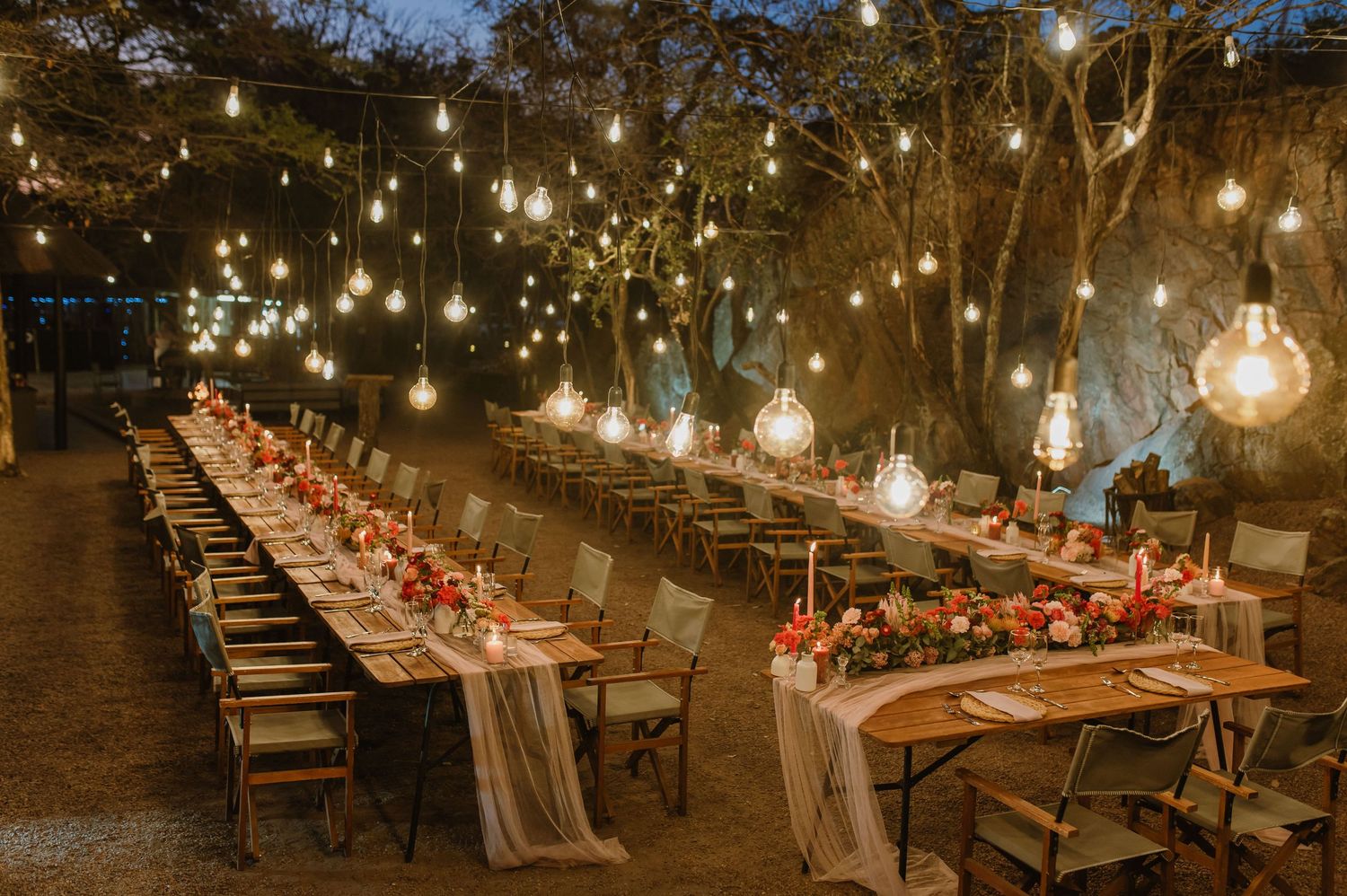 Overhead string lights illuminate long wedding reception tables in an outdoor setting.