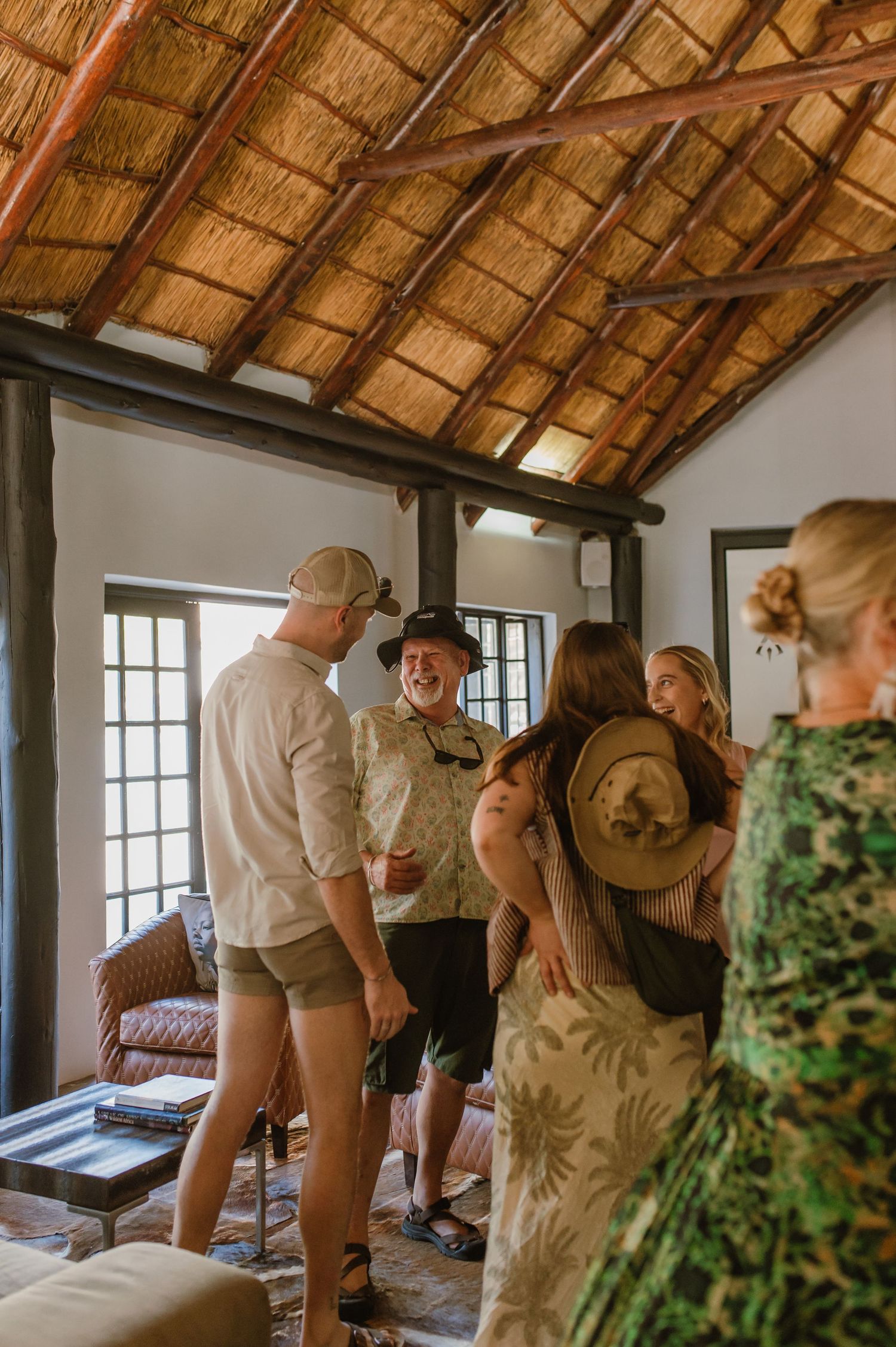 Guests mingling inside lodge with traditional thatched roof and wooden support beams.