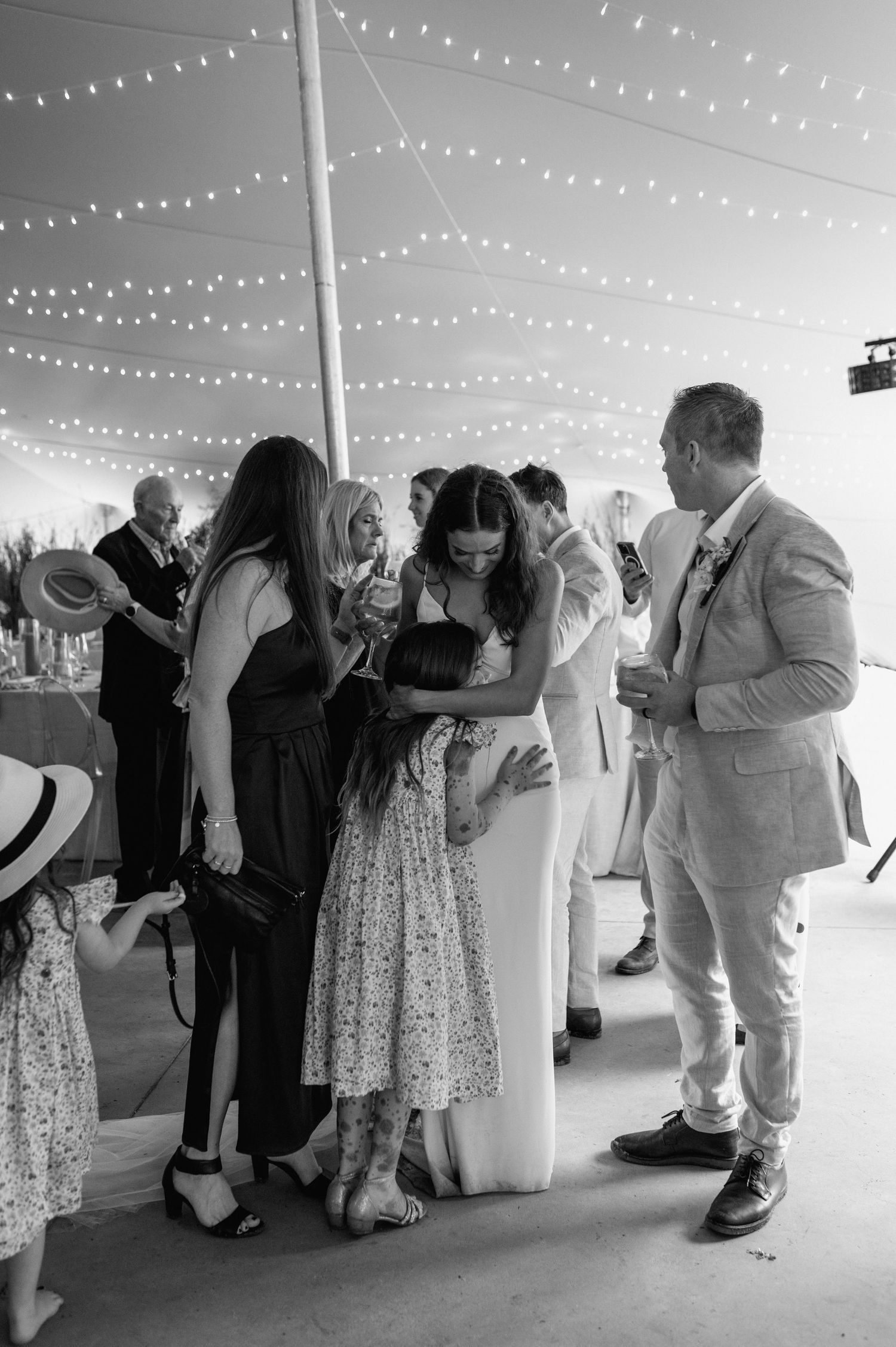 Black and white photo of couples dancing together under string lights at a wedding reception.