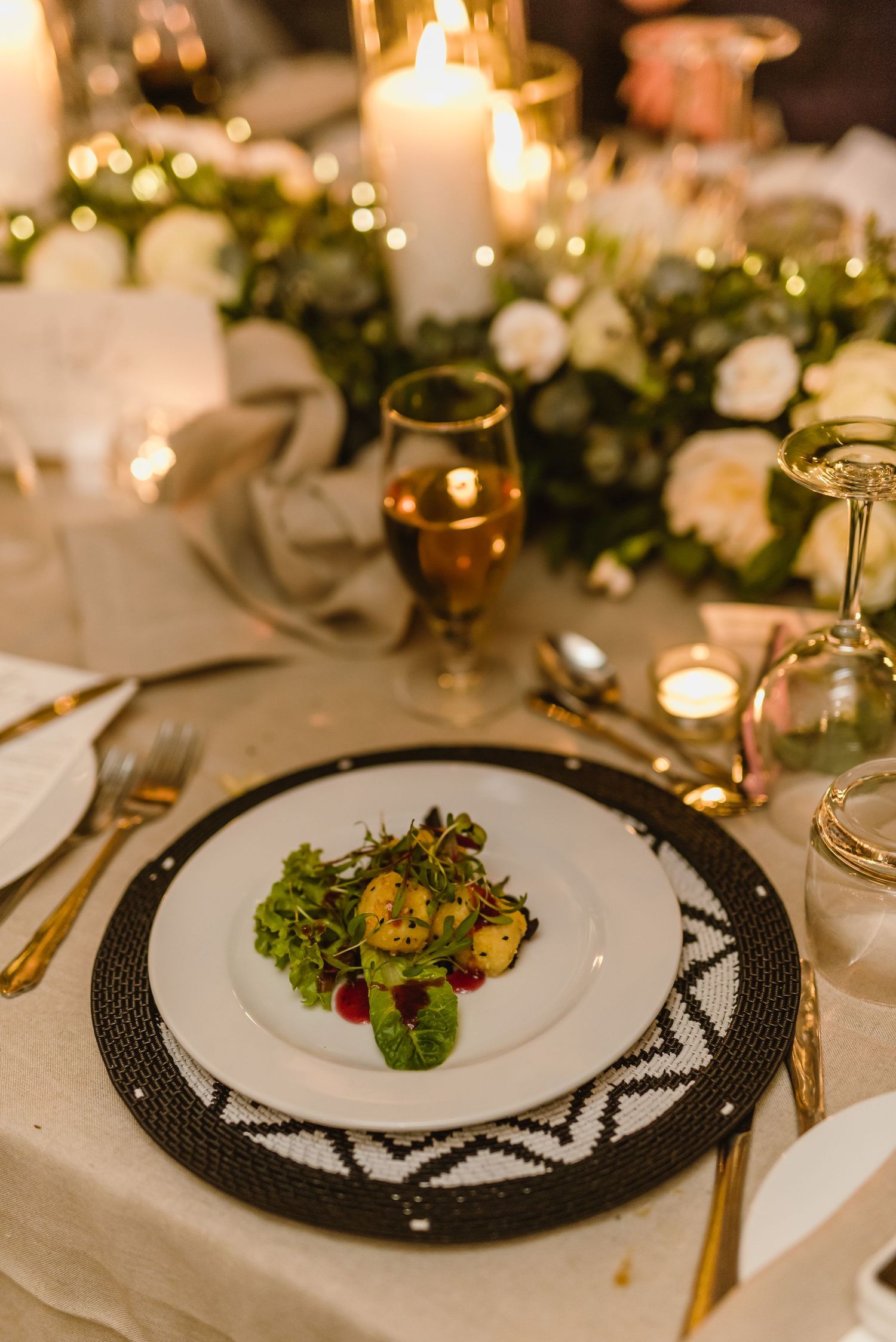 Elegant place setting with salad course on black and white charger plate at candlelit wedding reception.