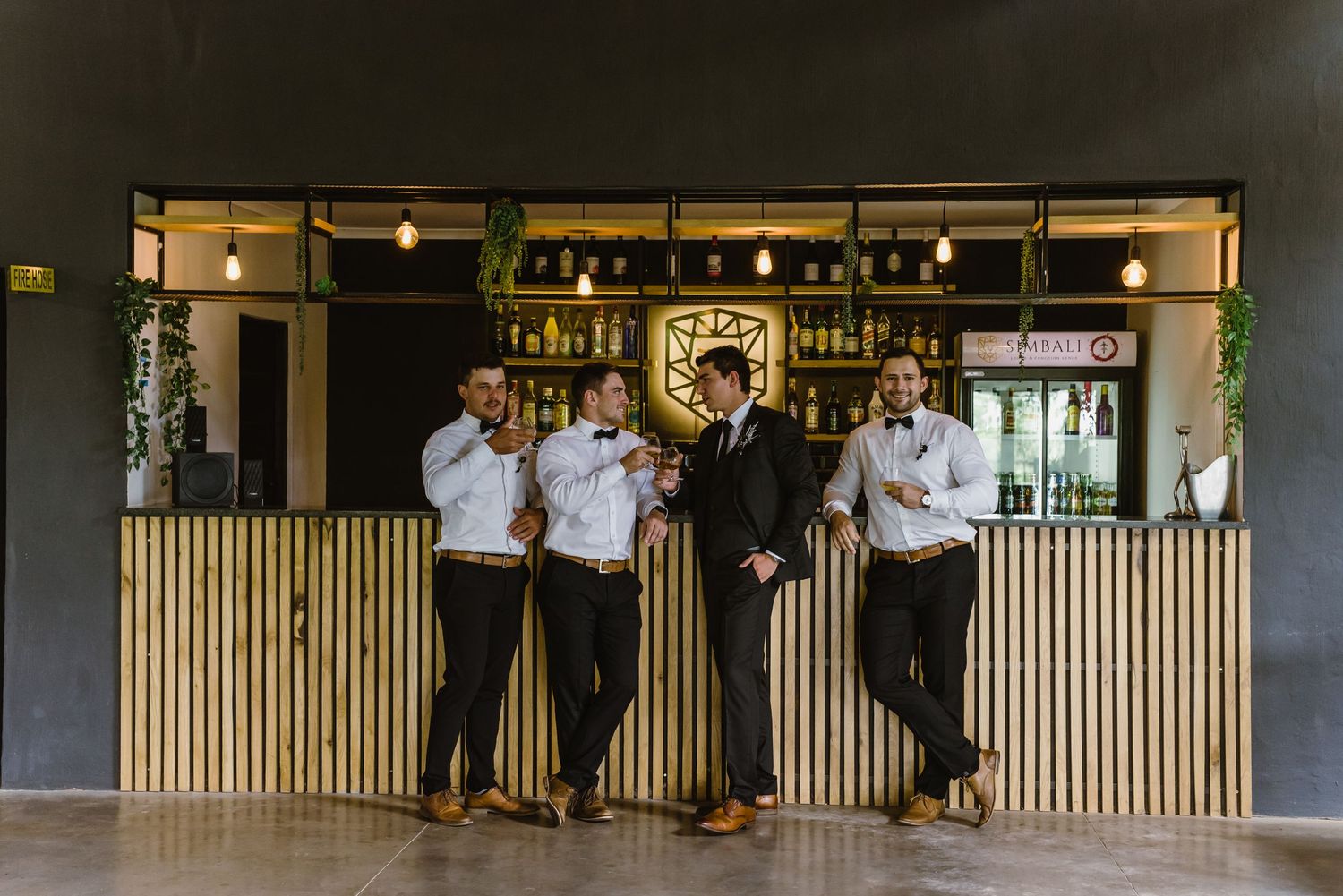 Wedding party members lined up at modern bar counter with wooden accents.