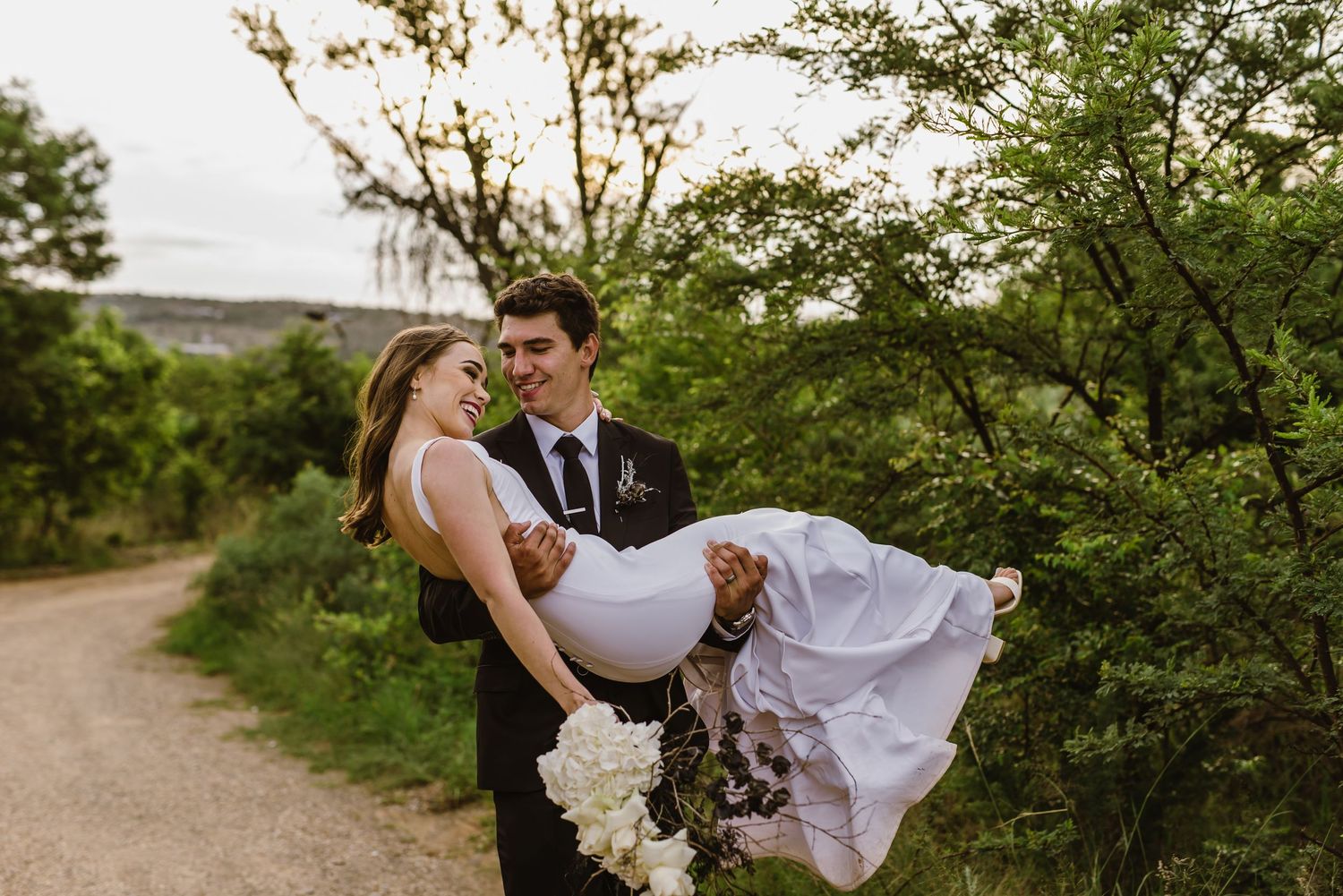 Wedding couple poses playfully with flowing dress on natural desert trail.