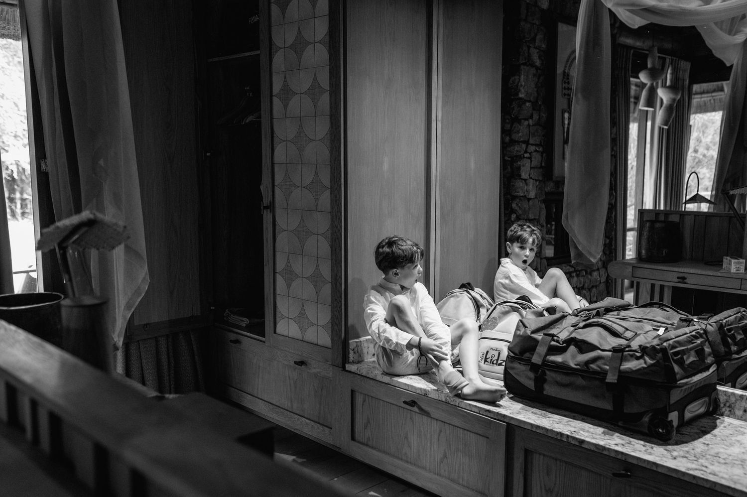 Black and white photo of two children sitting in a wooden locker room with luggage.