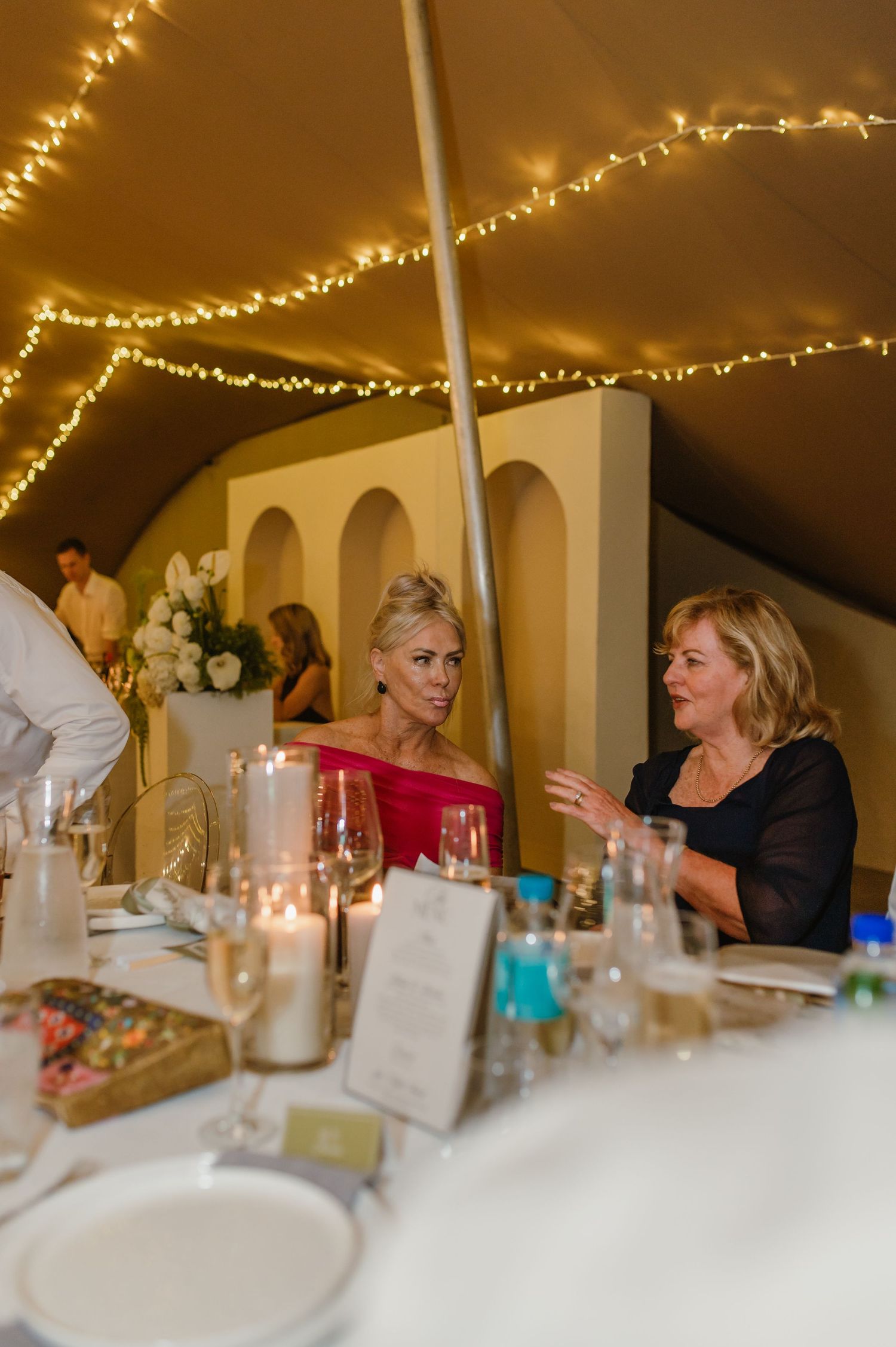Elegant wedding reception under string lights with guests seated at decorated tables.