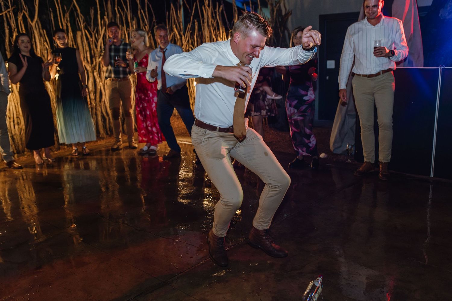 Guest dancing energetically on wet dance floor at outdoor evening wedding reception celebration.