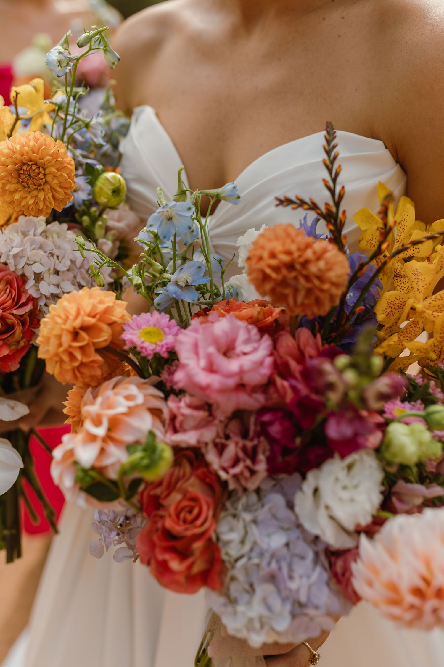 Close-up of a vibrant bridal bouquet featuring orange dahlias, pink roses, blue hydrangeas, and wildflowers.