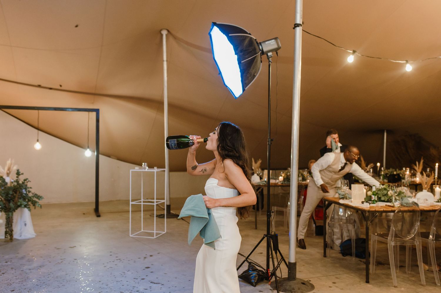 Wedding celebration in a tent venue with string lights and dancing guests.