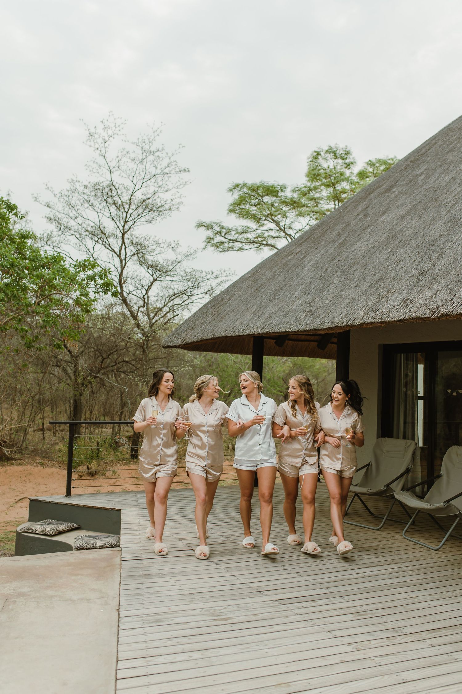 A group wearing matching silk pajama sets poses on a wooden deck at a luxury safari lodge.