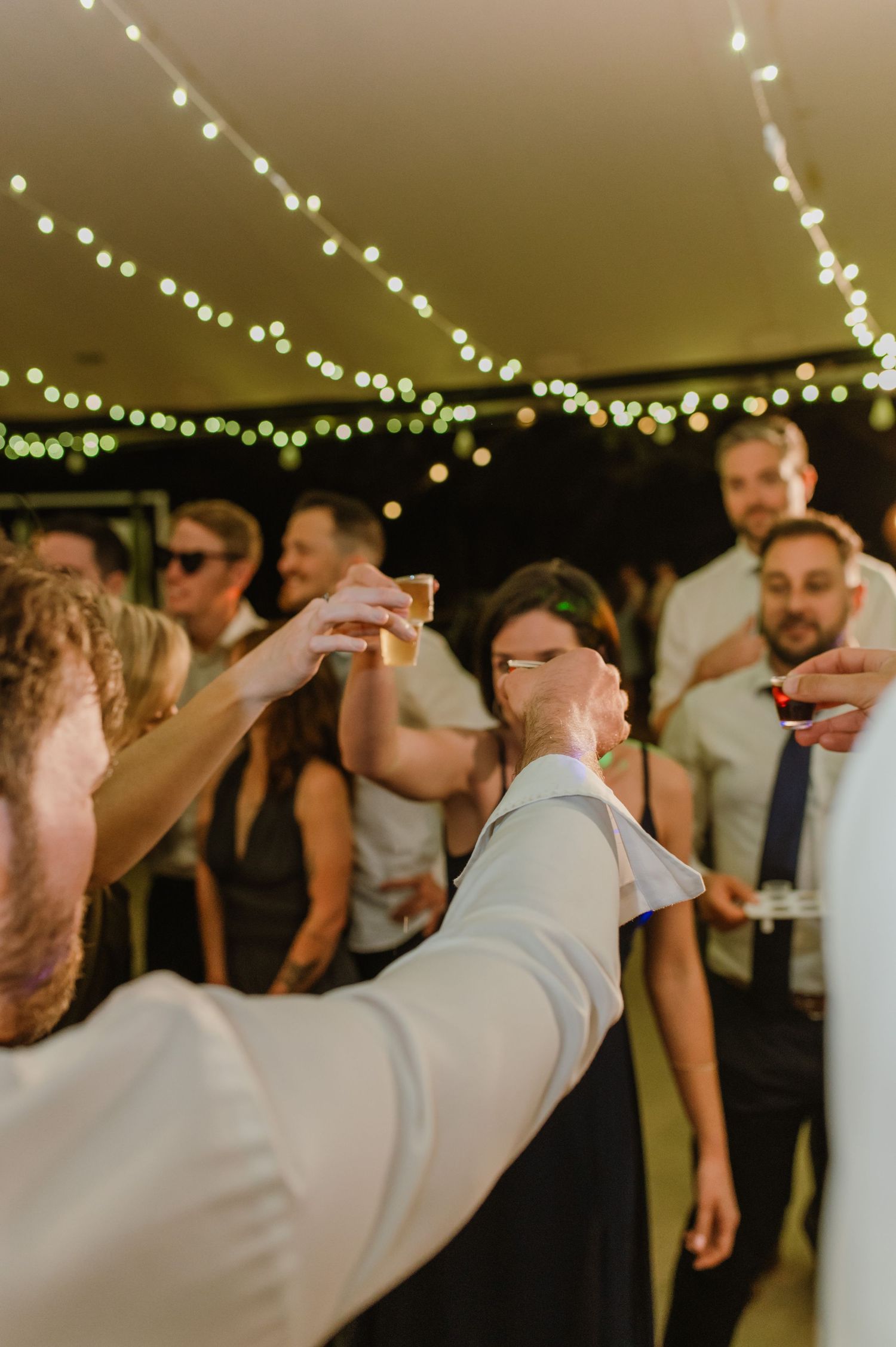 People dancing in silhouette under decorative string lights at an indoor event.
