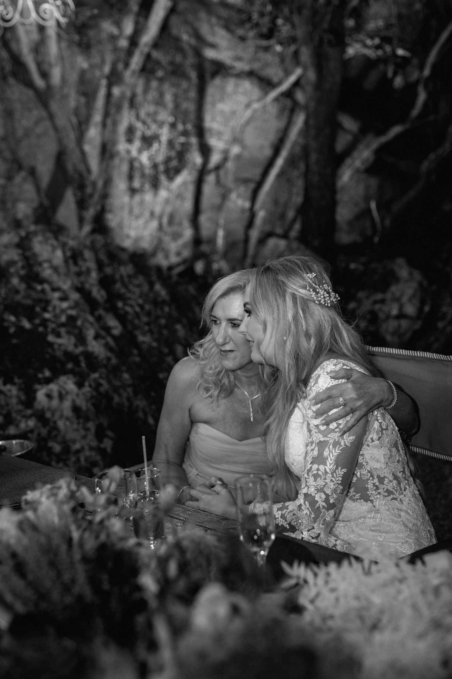 Black and white photo of two guests seated at elegant outdoor reception table with floral arrangements.