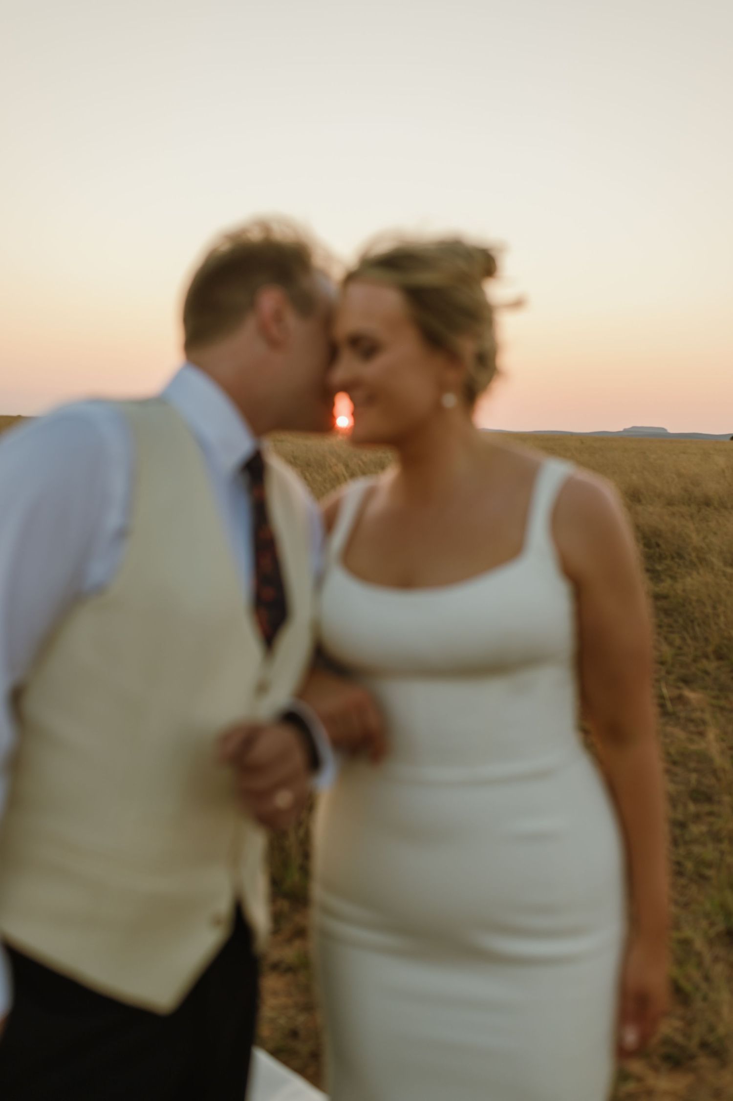 A couple shares a romantic moment at sunset in an outdoor field setting.