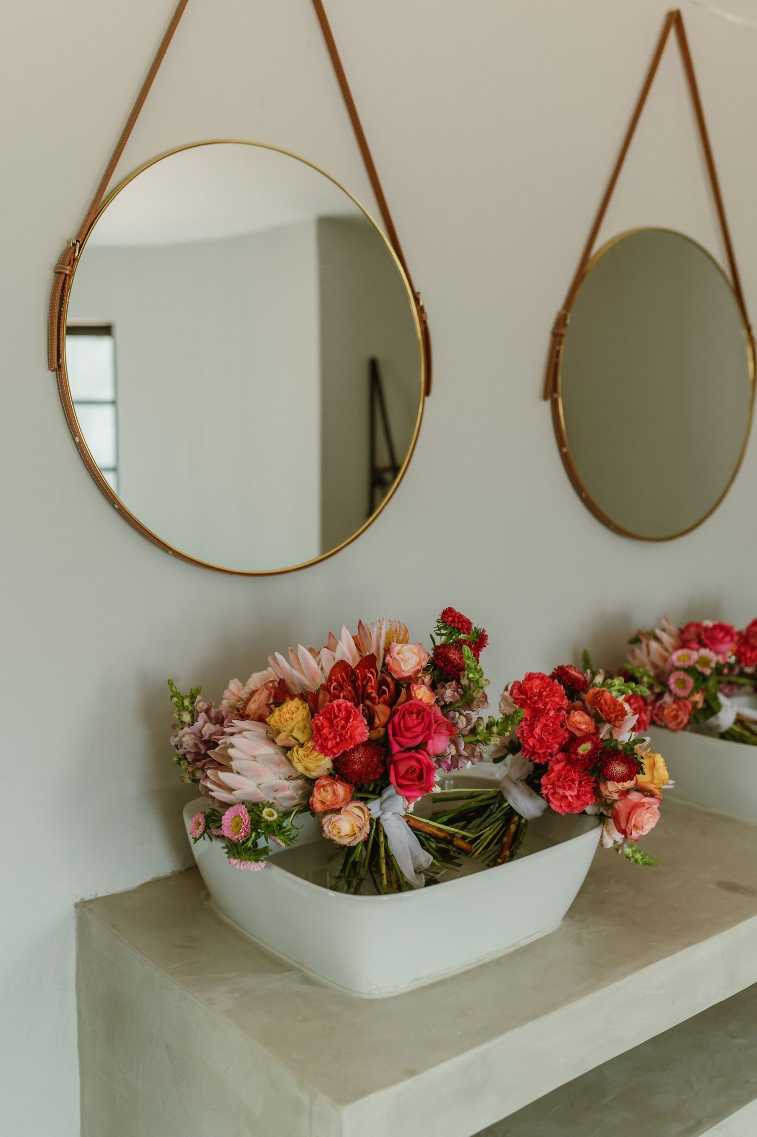 Modern vanity setup with circular mirrors and vibrant flower arrangements.