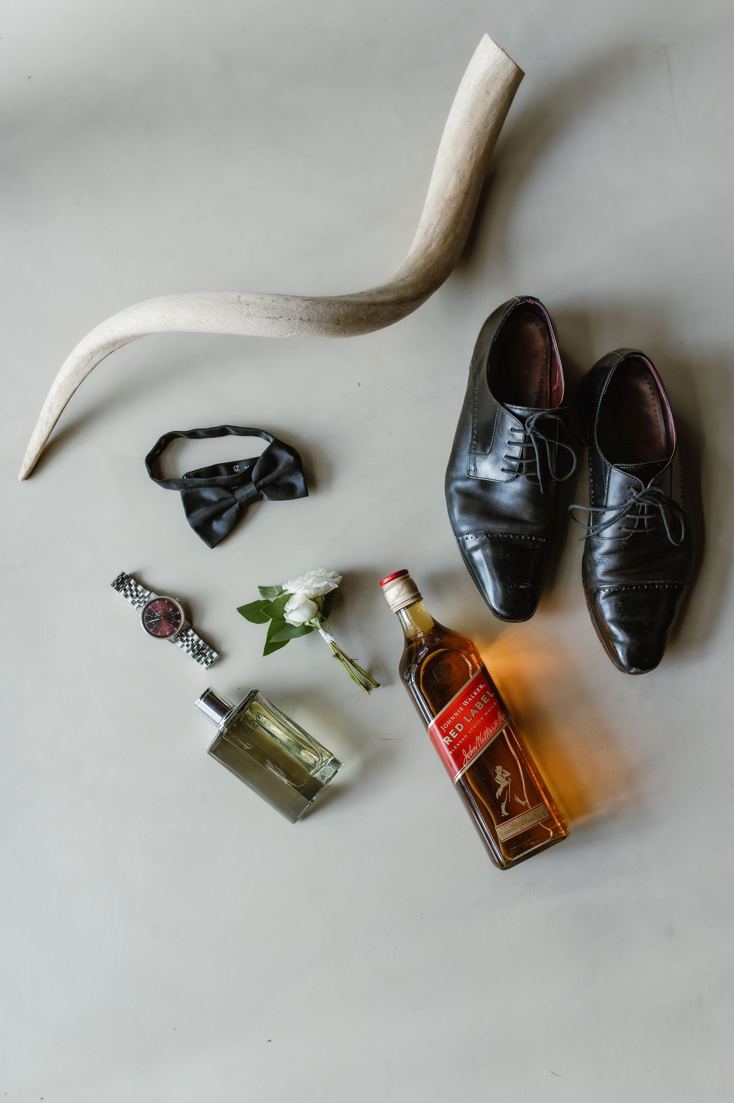 Wedding accessories including dress shoes, cologne bottles, and decorative items arranged on light background.