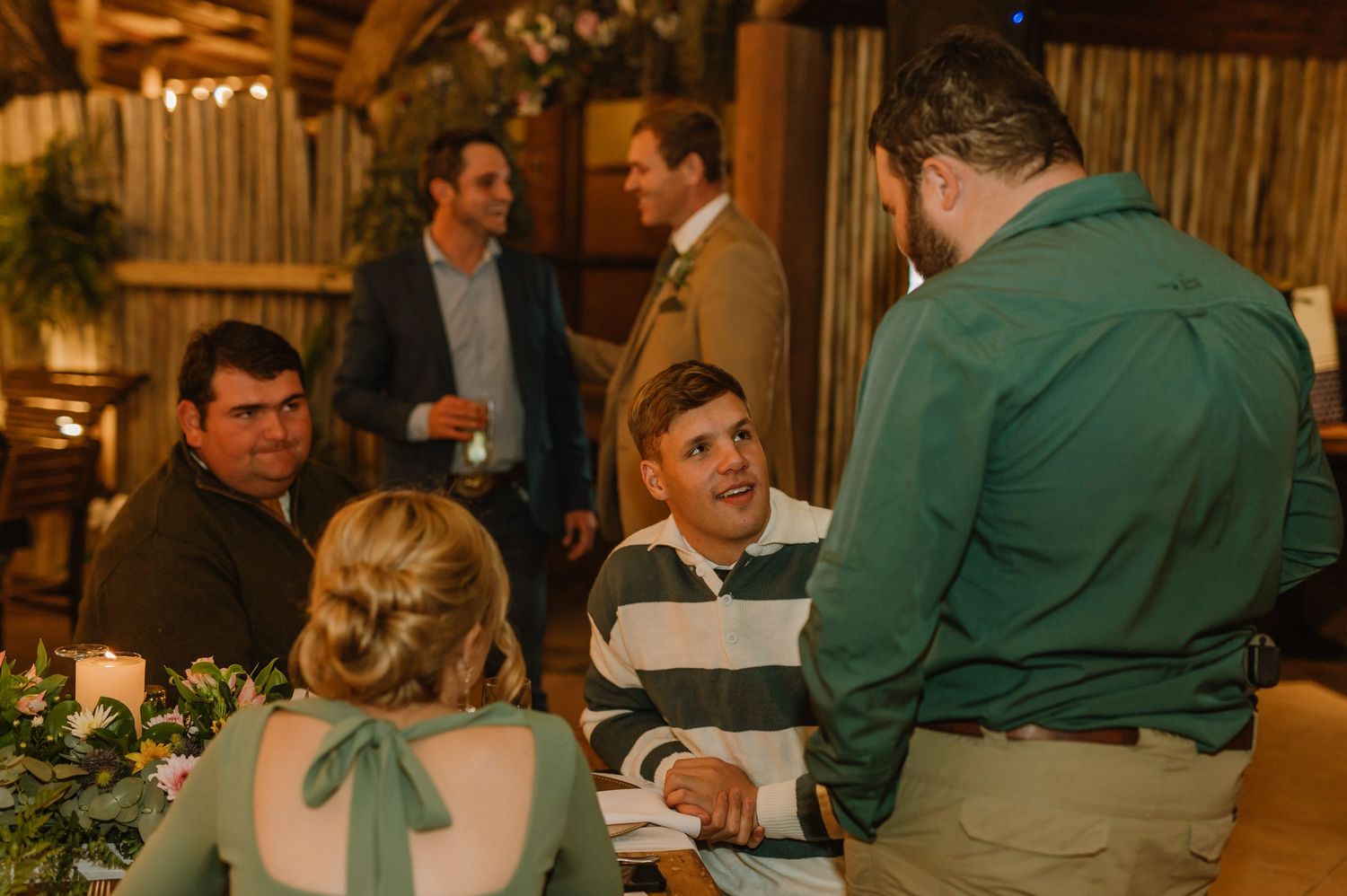 Guests mingle and socialize at a rustic barn wedding reception under warm lighting and wooden beams.