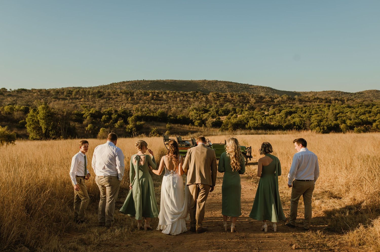 Wedding group photo in panoramic view with mountains and golden grass at sunset.