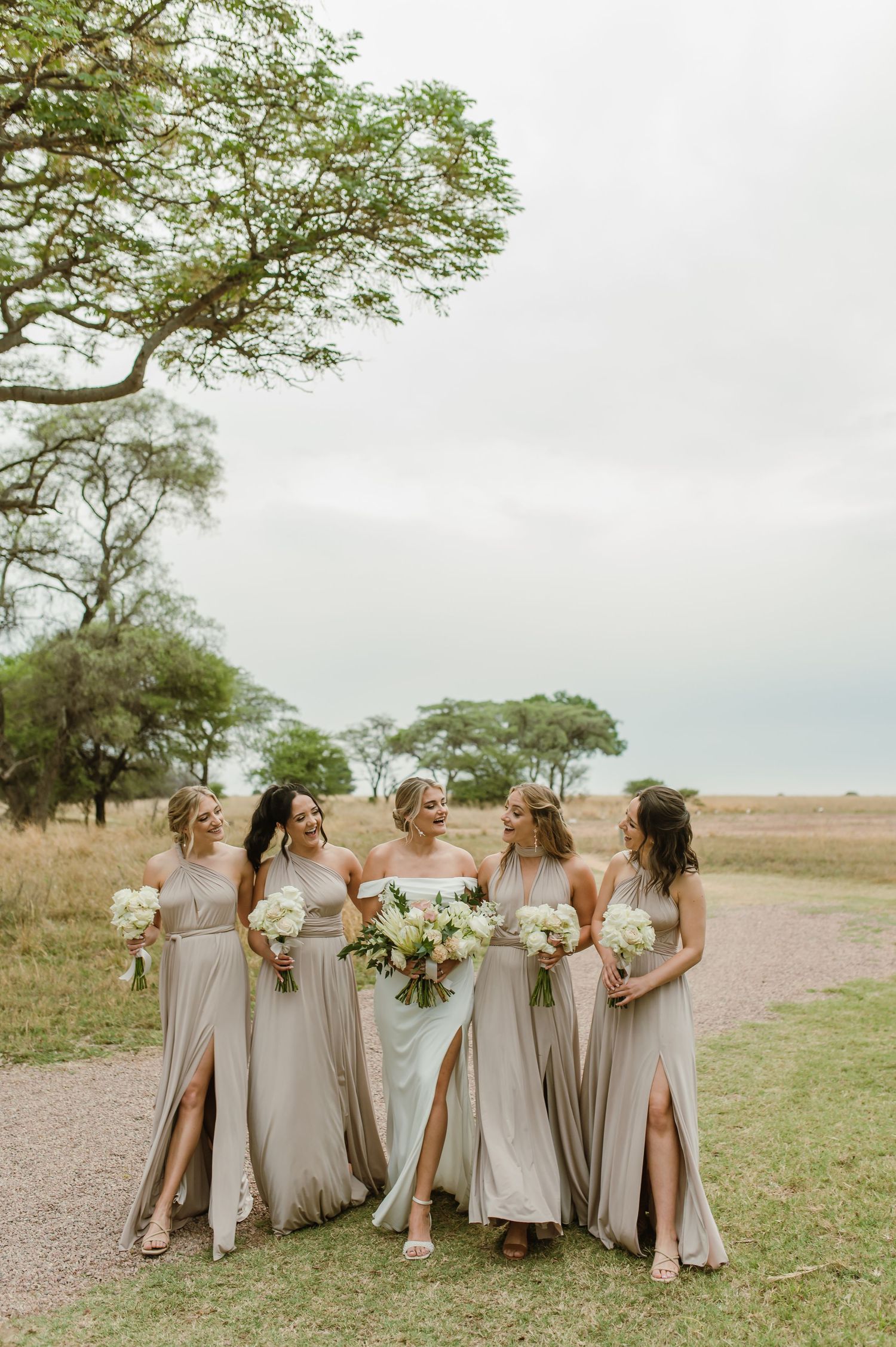 Wedding party in neutral dresses walking together across an open field.