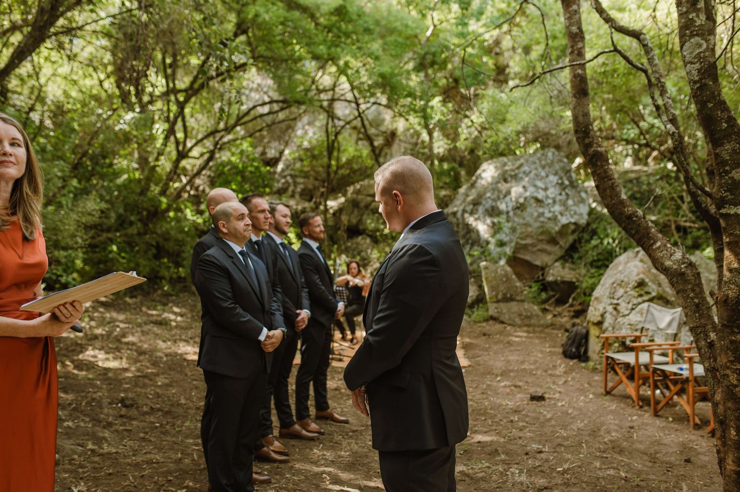 Wedding party members lined up along a rustic forest path during ceremony.
