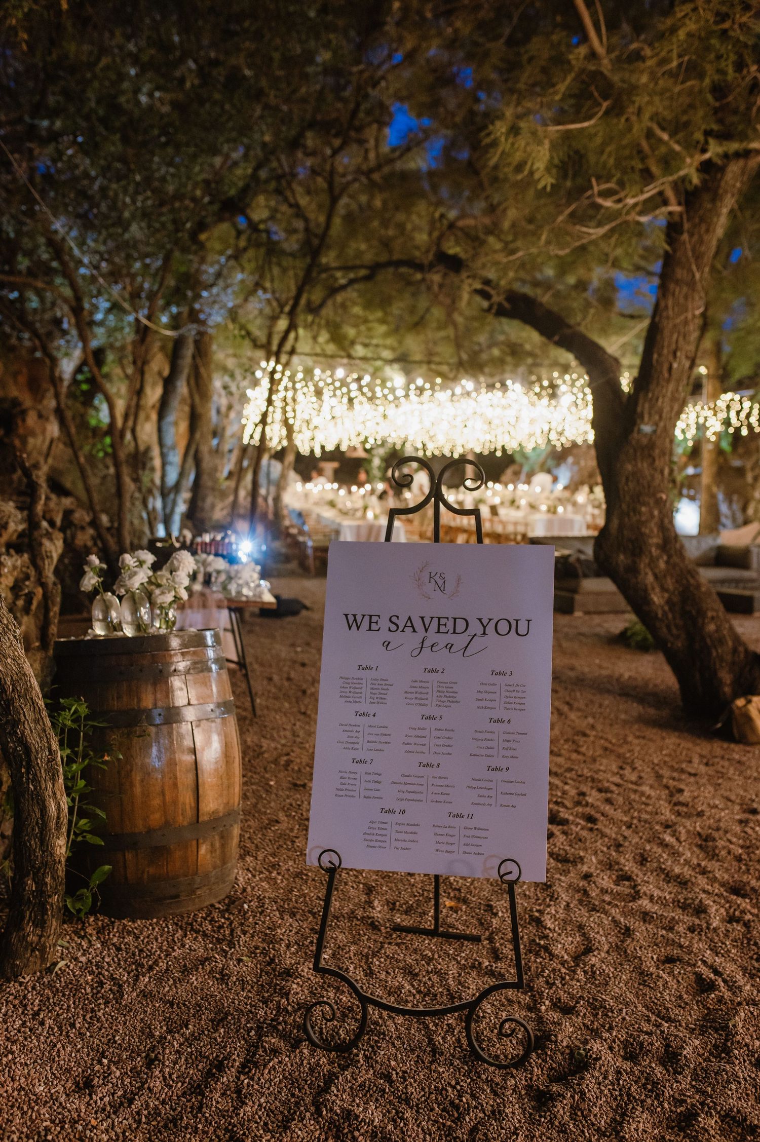 Wedding reception seating chart and signage illuminated by string lights at dusk.