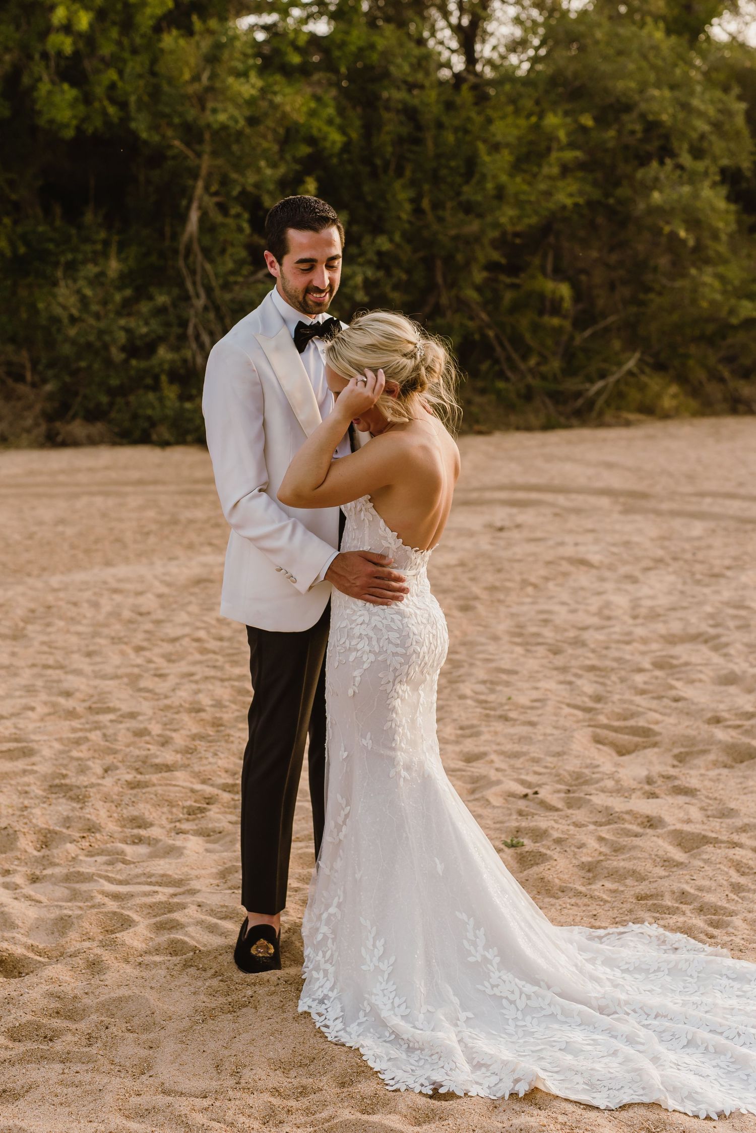 Beautiful lace wedding dress train flows across sandy beach during sunset portraits.