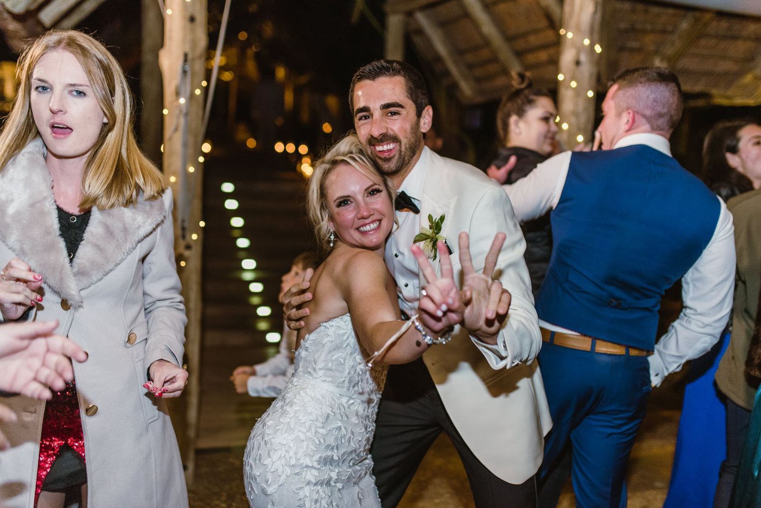 Wedding party dancing and celebrating in a rustic barn setting with festive lighting.