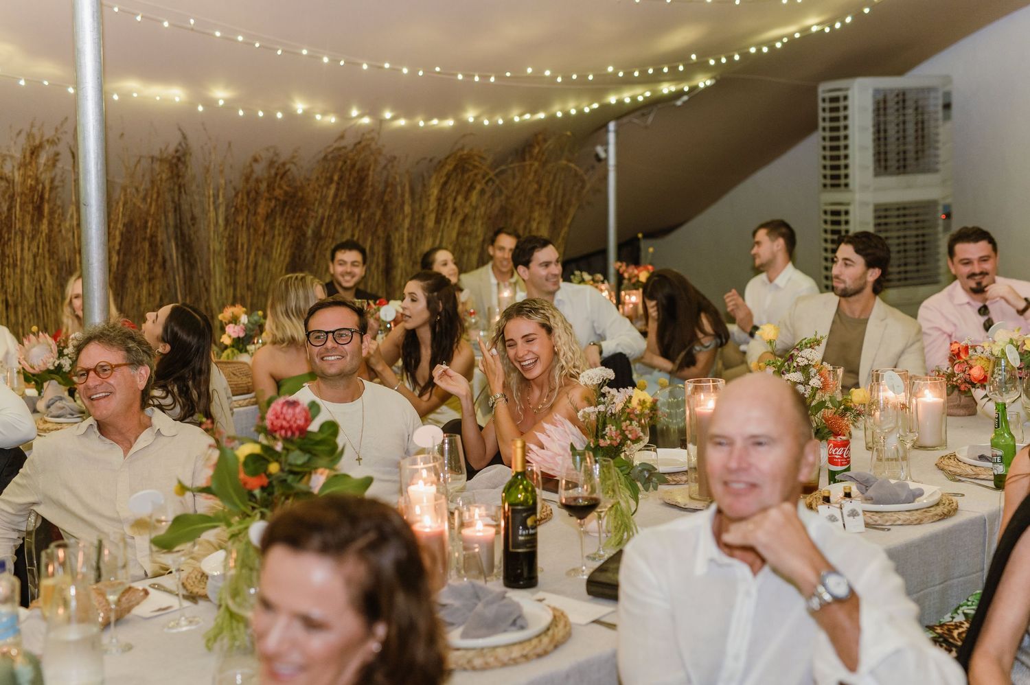 Reception guests enjoying dinner at decorated tables under glowing tent lighting.
