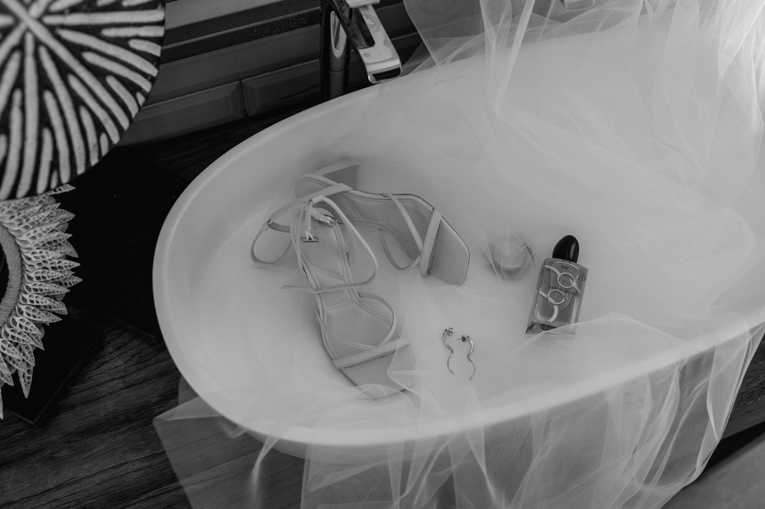 Wedding details including white shoes, perfume bottle, and delicate jewelry arranged on tulle fabric.