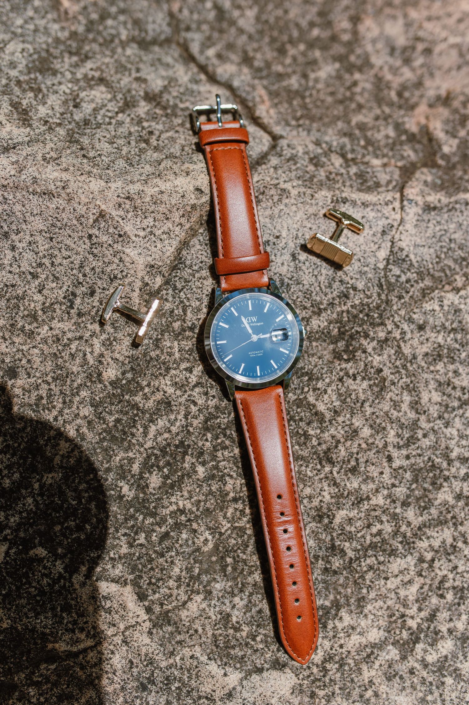 Classic wristwatch with brown leather strap and navy blue face on concrete surface.