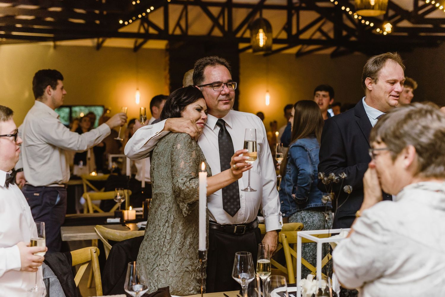 Wedding guests mingle and celebrate during the reception under warm lighting.