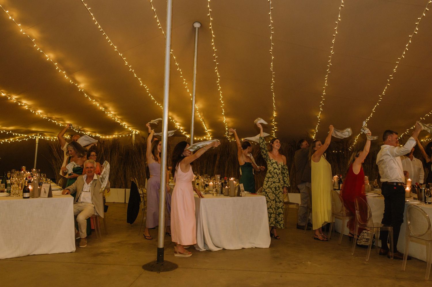 Wedding reception dance floor filled with guests under warm string lights in a tent.