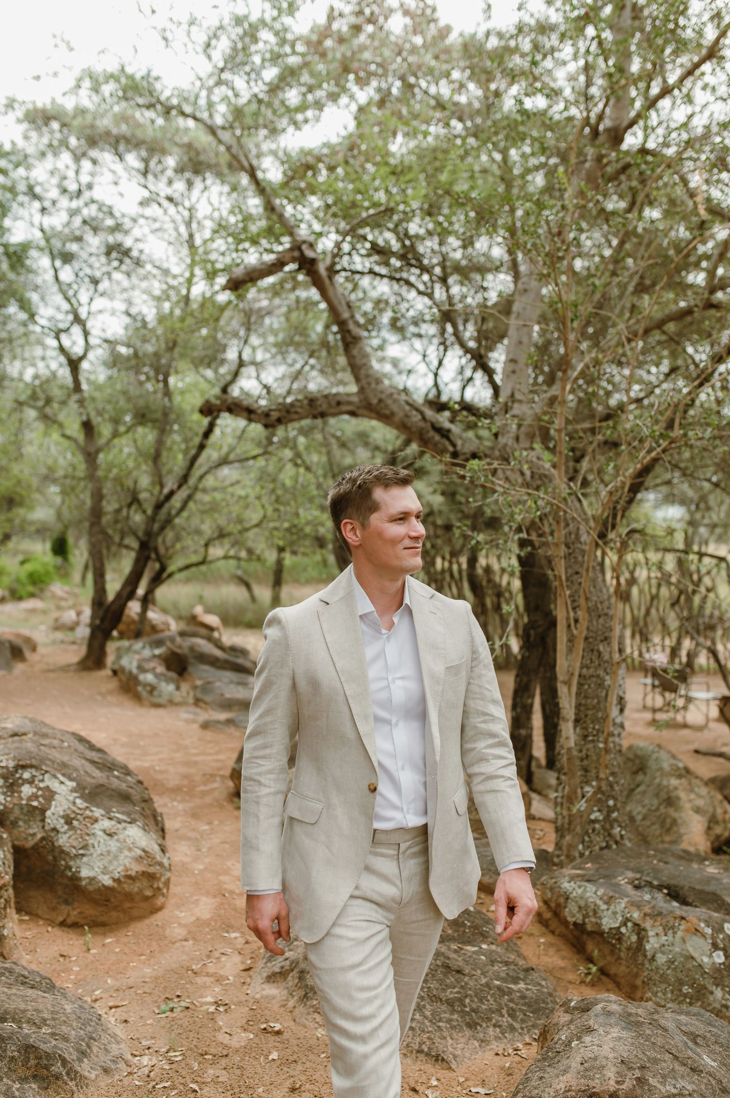Person in light suit walking along rocky path surrounded by trees in natural setting.