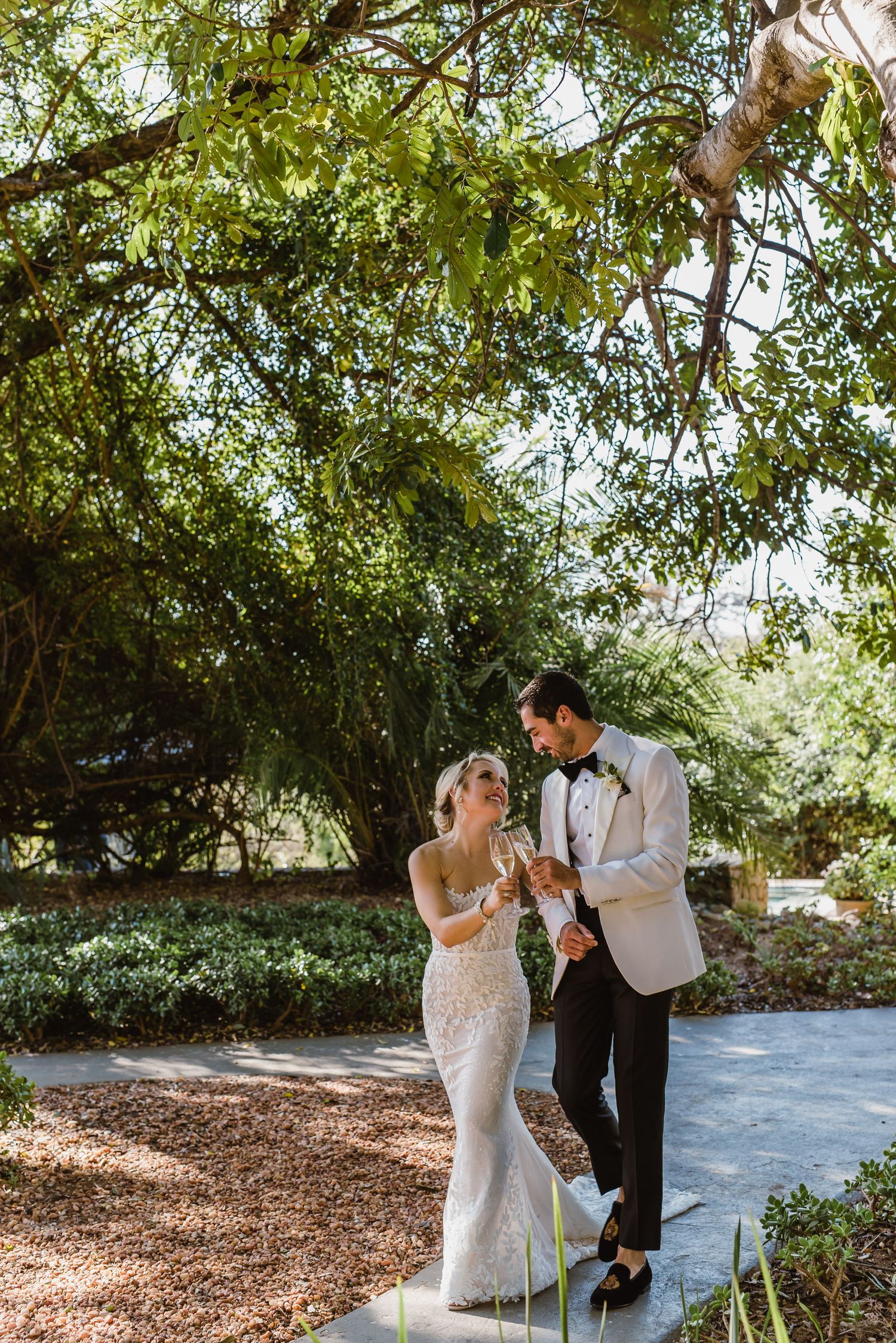 A couple shares a romantic moment under lush green trees on their wedding day.