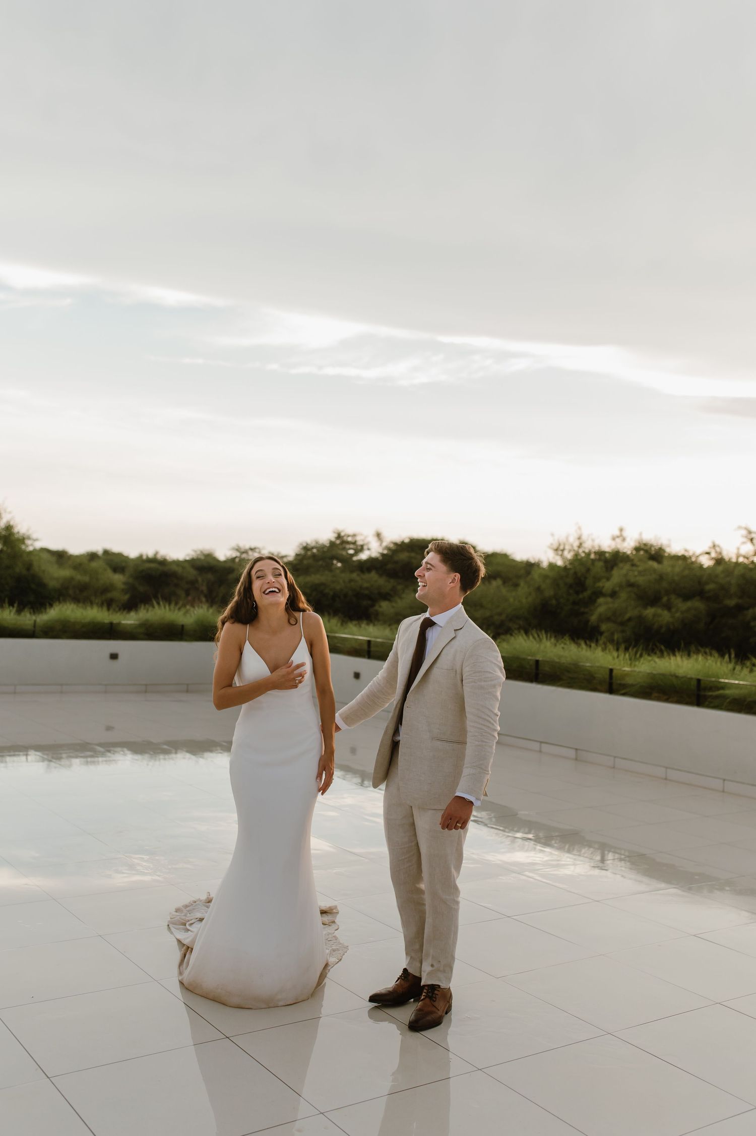 A couple in wedding attire sitting and laughing on a white modern terrace.