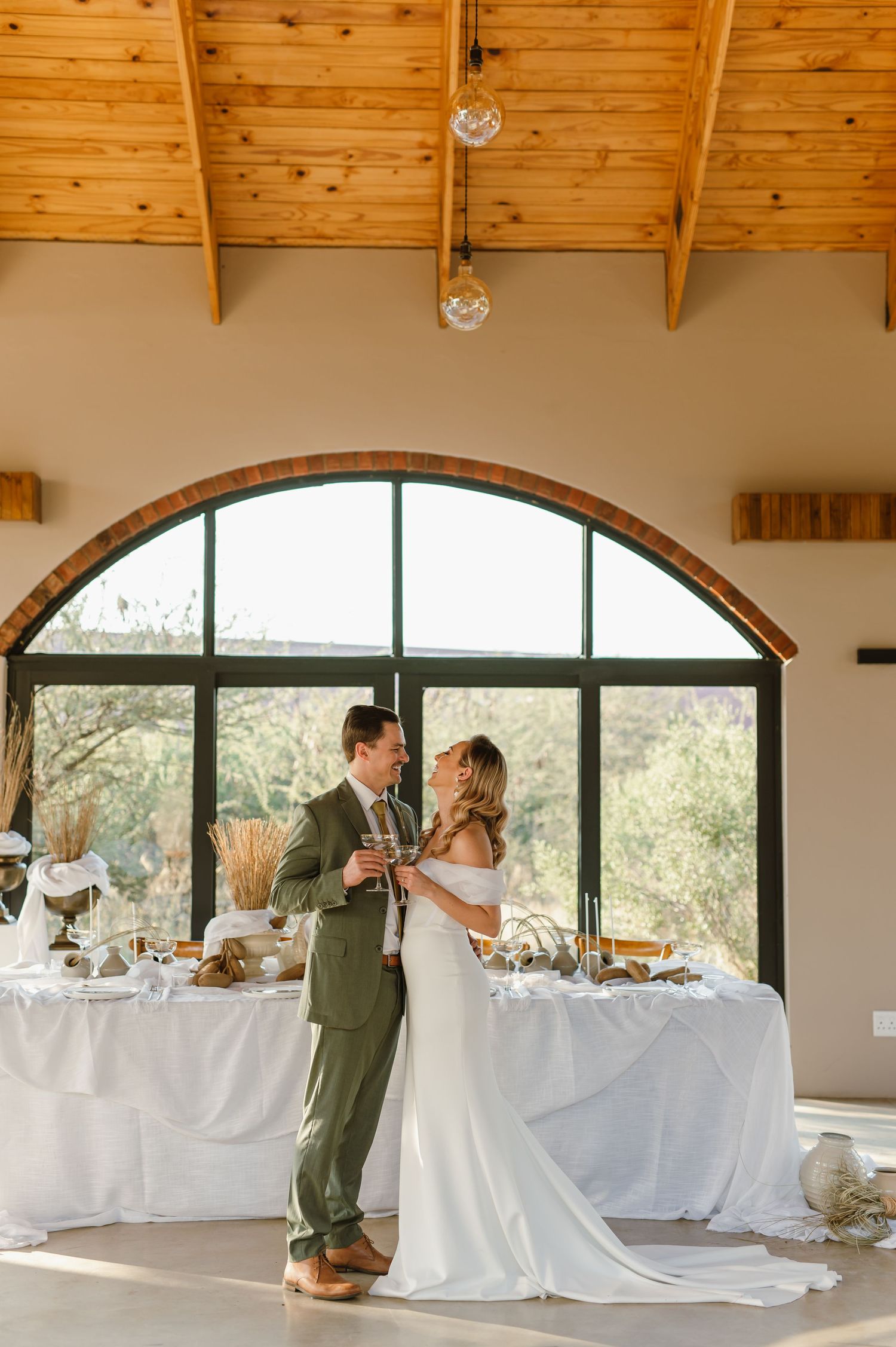 Light-filled reception venue with wooden ceiling beams and white-draped tables.