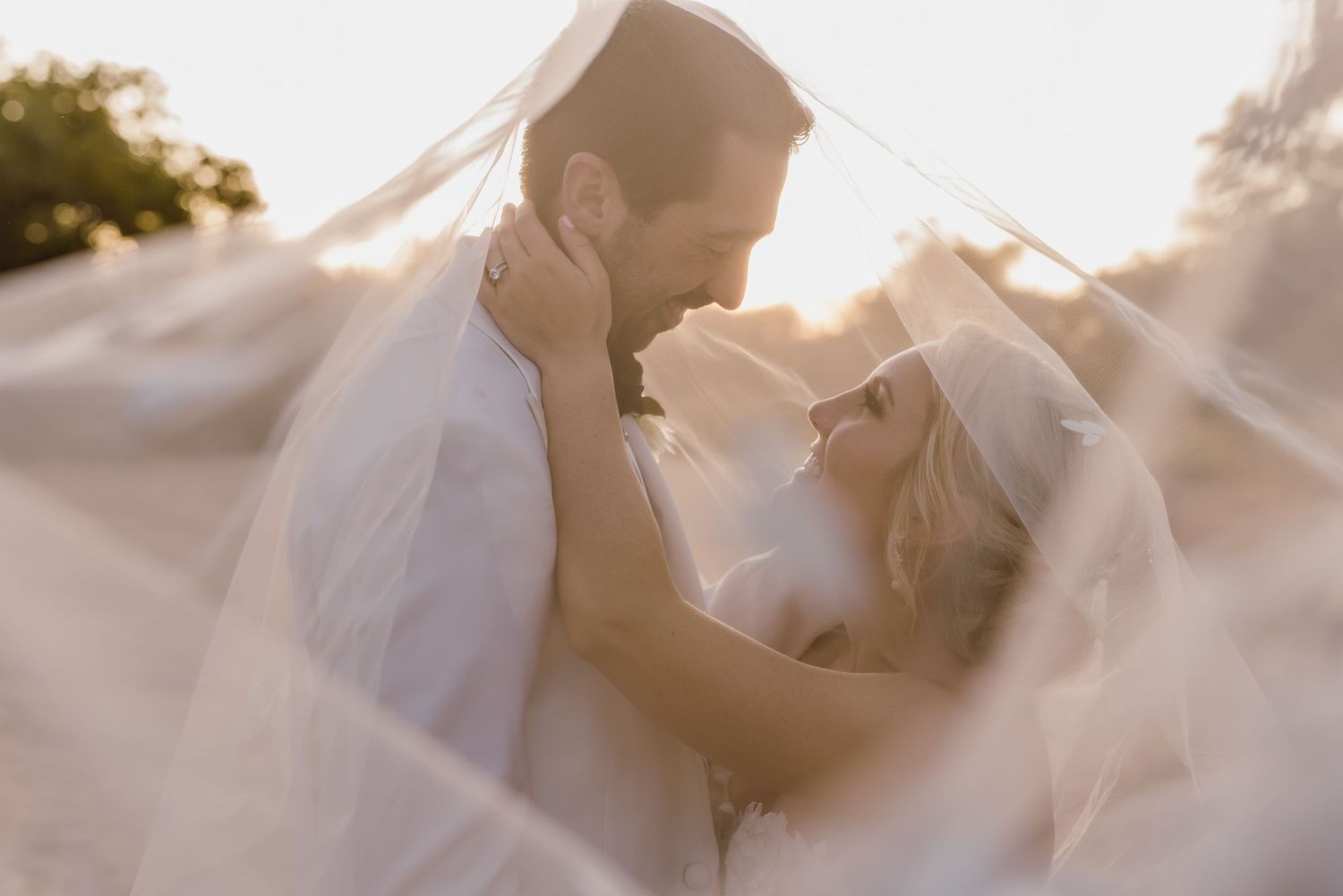 Intimate wedding portrait of couple embracing on sandy beach during sunset.