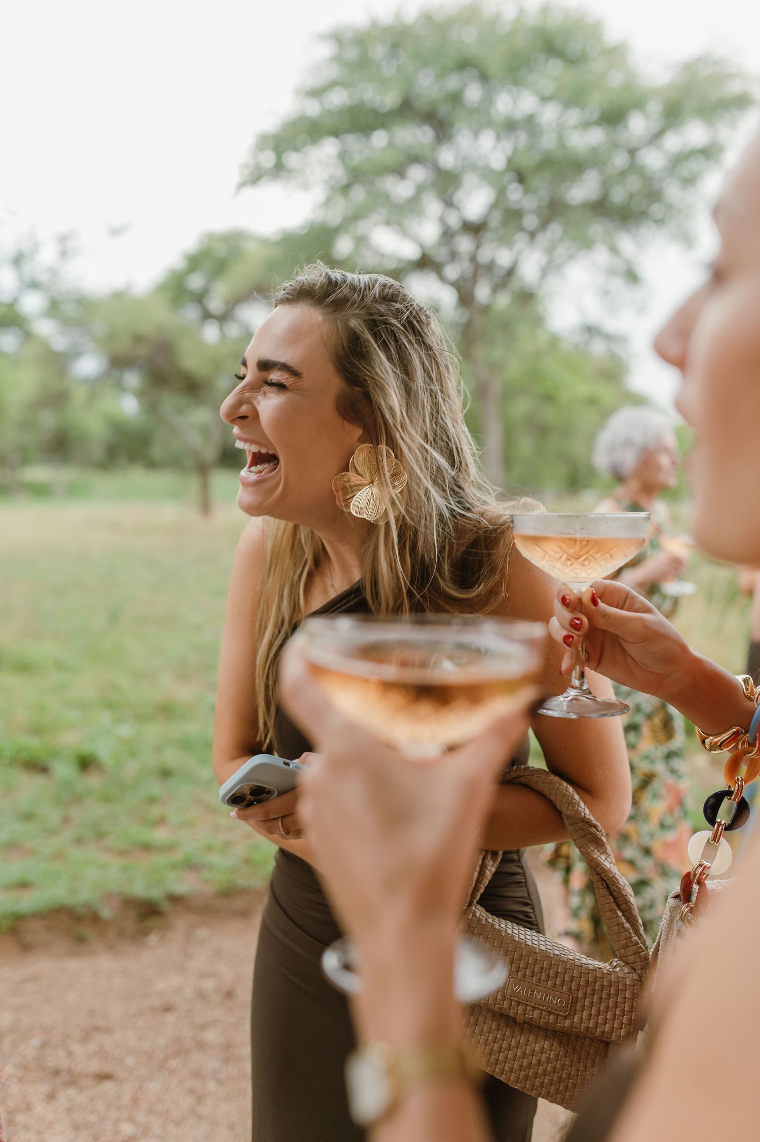 Wedding guests laugh while holding champagne glasses at outdoor reception.