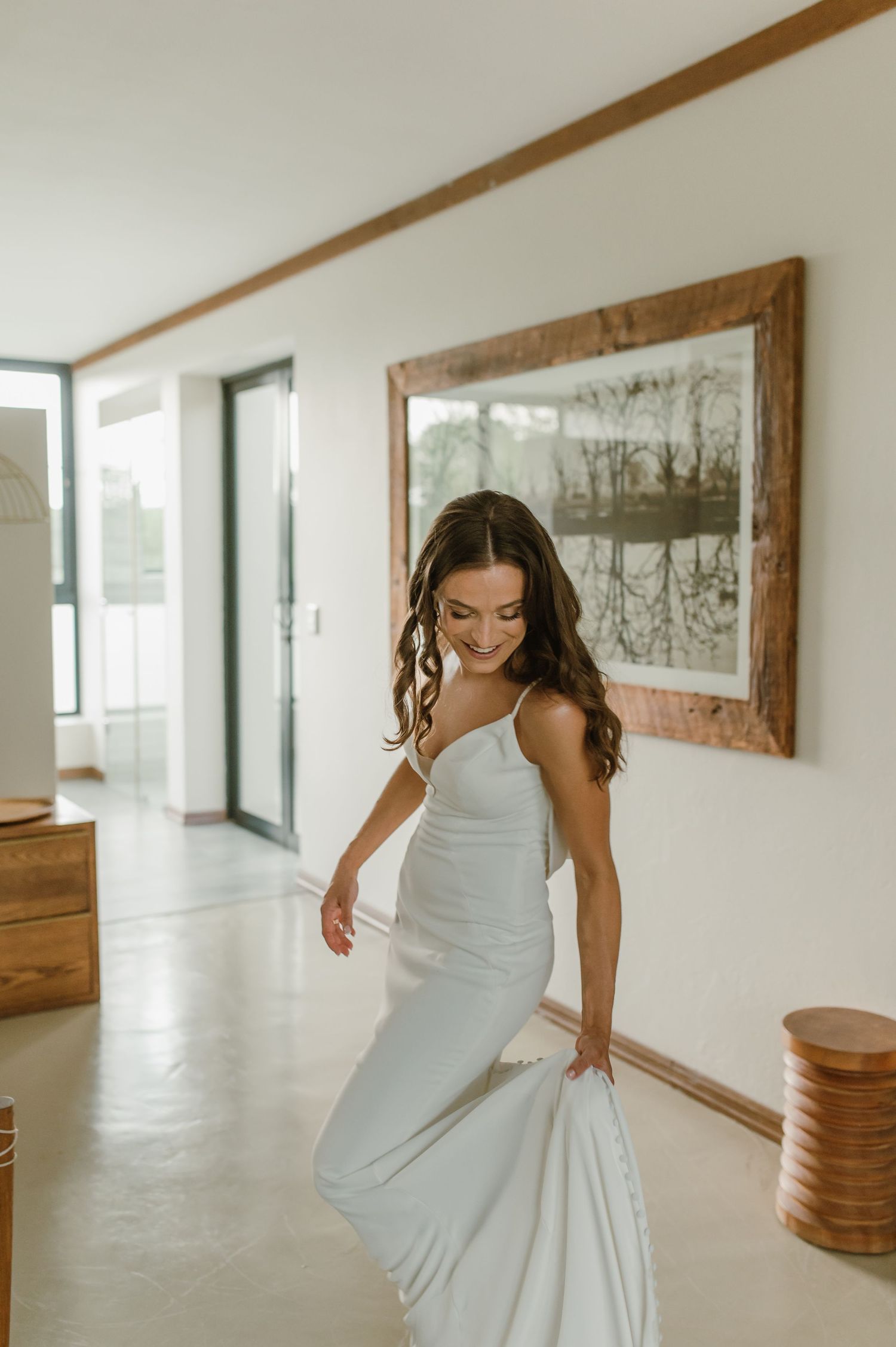 A person in white twirls through a minimalist hallway with wooden accents and framed artwork.
