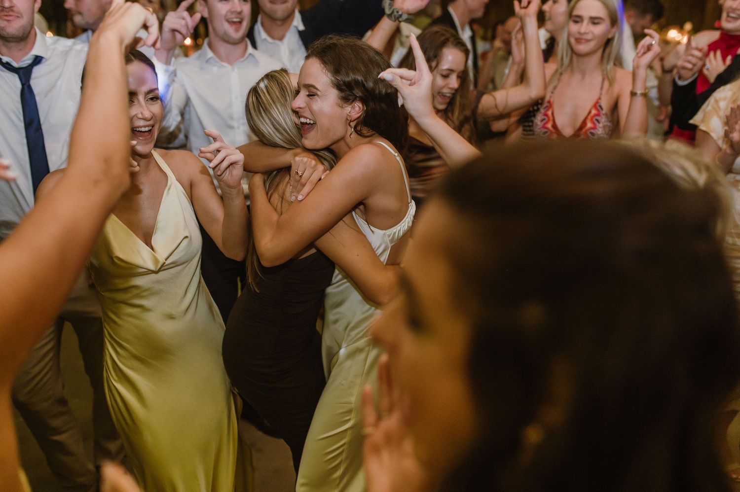 Joyful celebration on the dance floor with wedding guests under warm lighting.