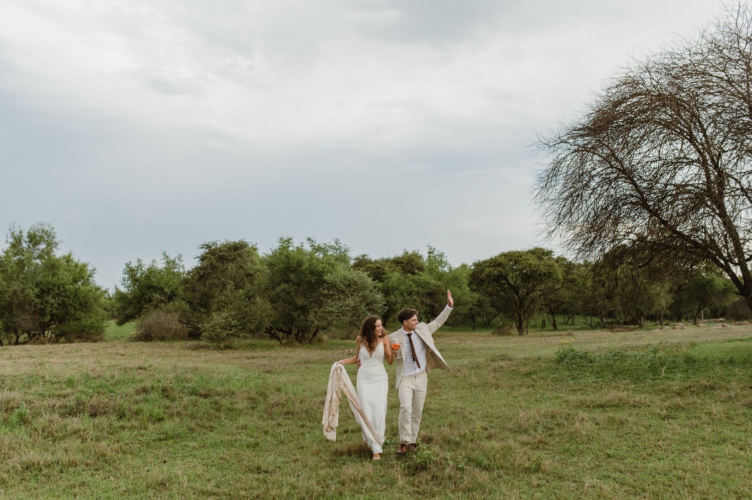Newlyweds celebrate with raised arms while walking through a scenic outdoor field.