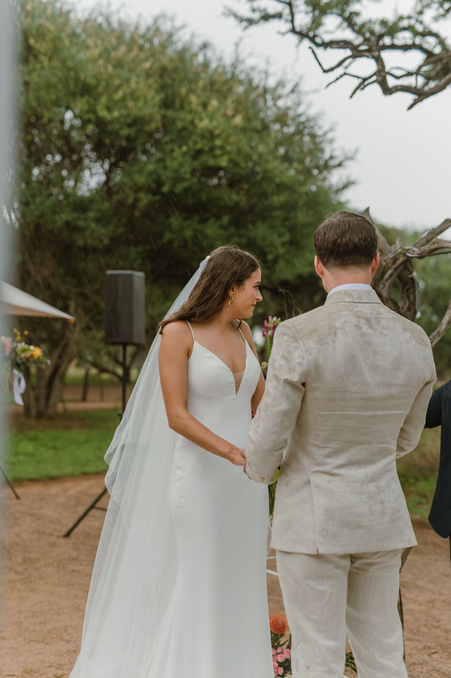 Couple walks together on a rustic dirt path under trees at an outdoor wedding ceremony.