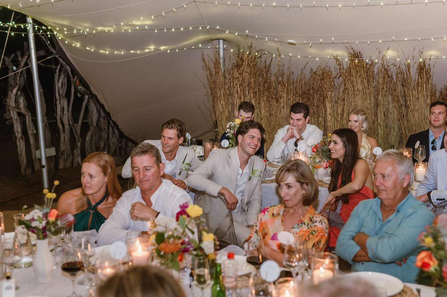 Wedding guests seated at long tables during an evening outdoor reception with ambient lighting.