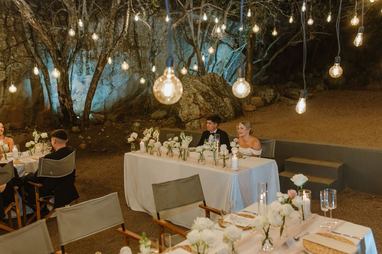 Long dining tables set up outdoors with hanging string lights creating a romantic ambiance.