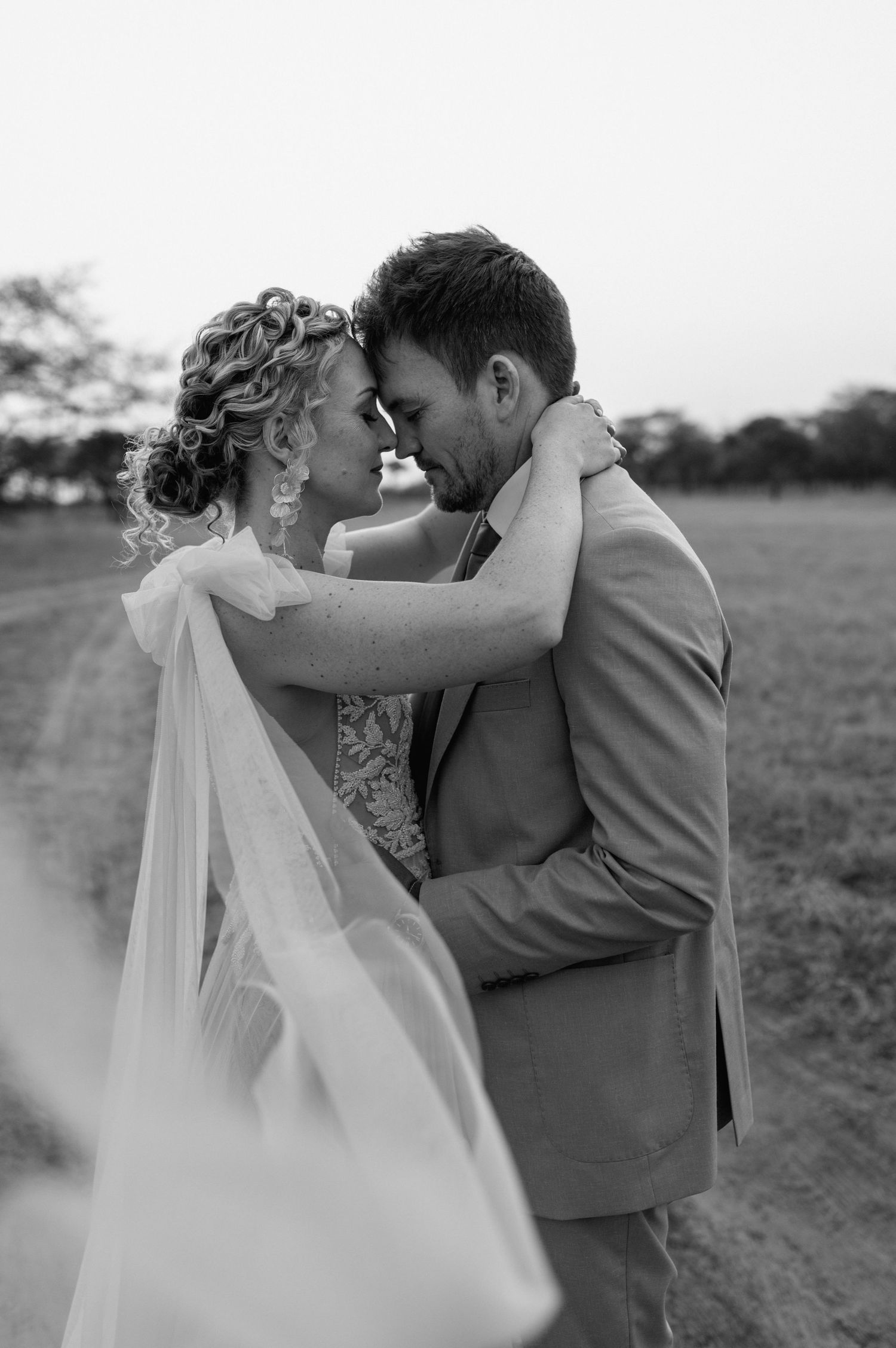 Black and white wedding portraits capture intimate moments between newlyweds in an outdoor setting.