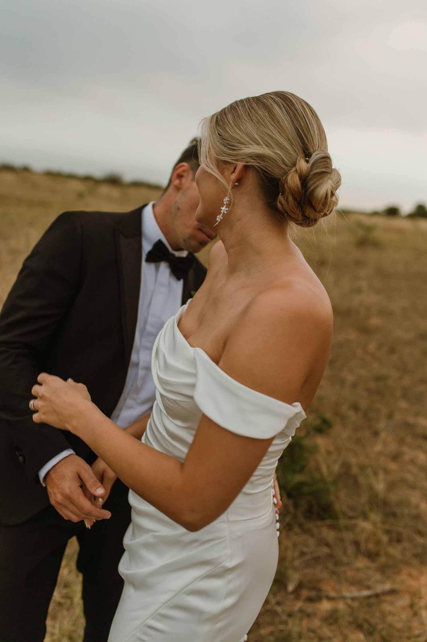 Romantic wedding portraits in golden field showcase elegant bridal gown.