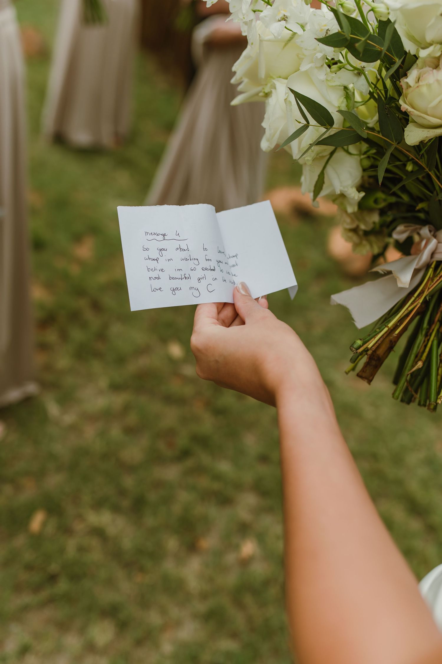 Hand holding small handwritten note card against white wedding bouquet.